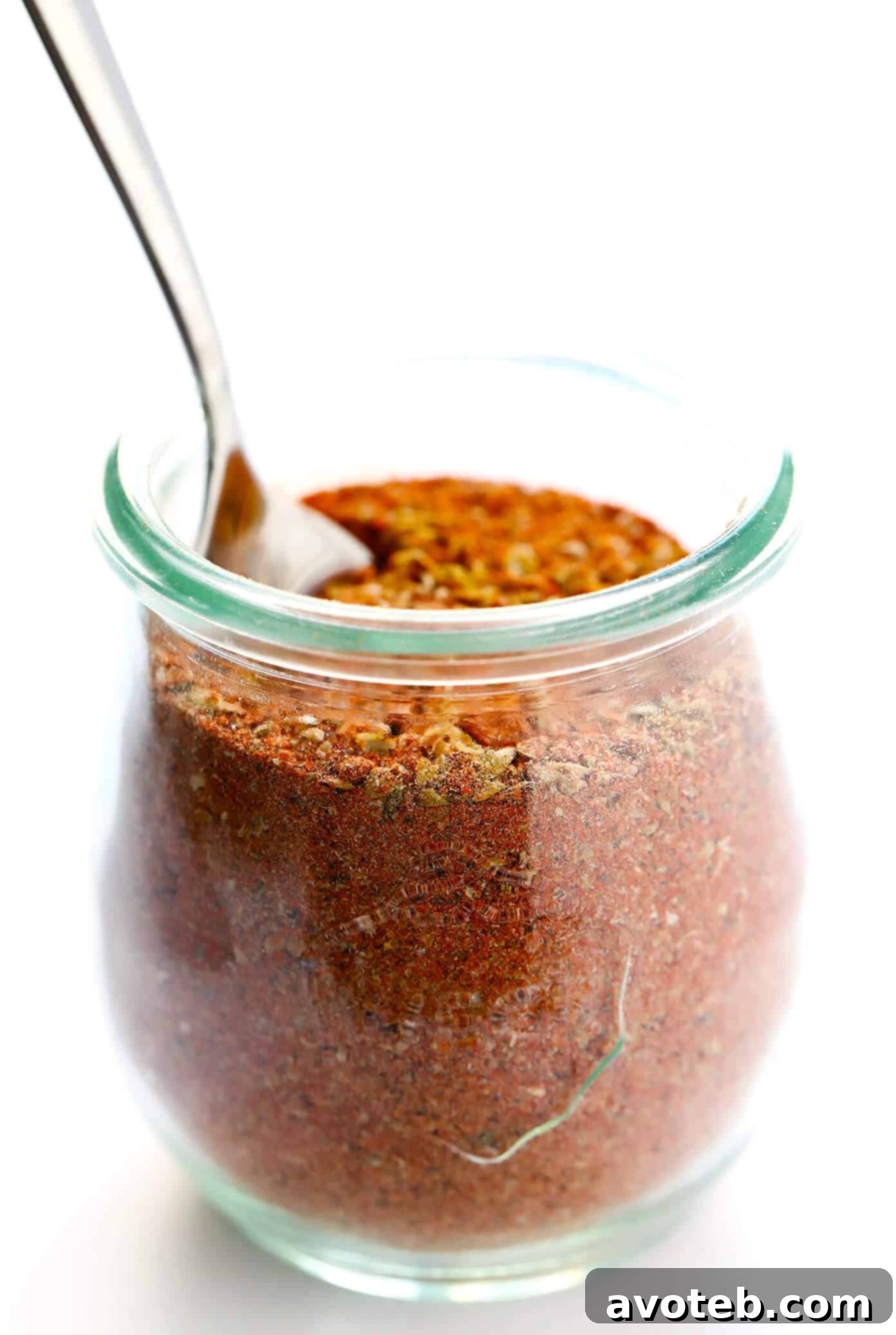 A glass jar filled with homemade Cajun seasoning, ready for use, sits on a rustic surface.