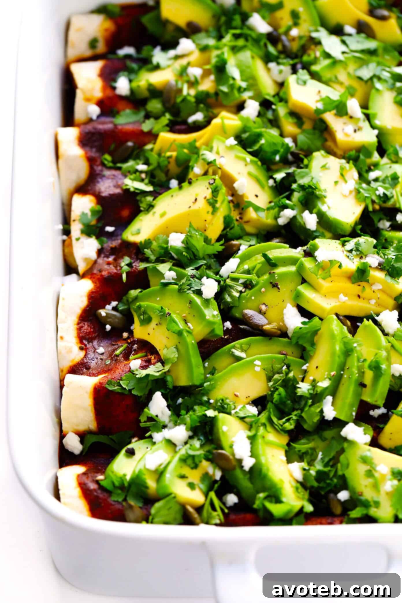 A close-up of a single Roasted Cauliflower Enchilada, generously topped with fresh avocado, cilantro, and crumbled queso fresco.