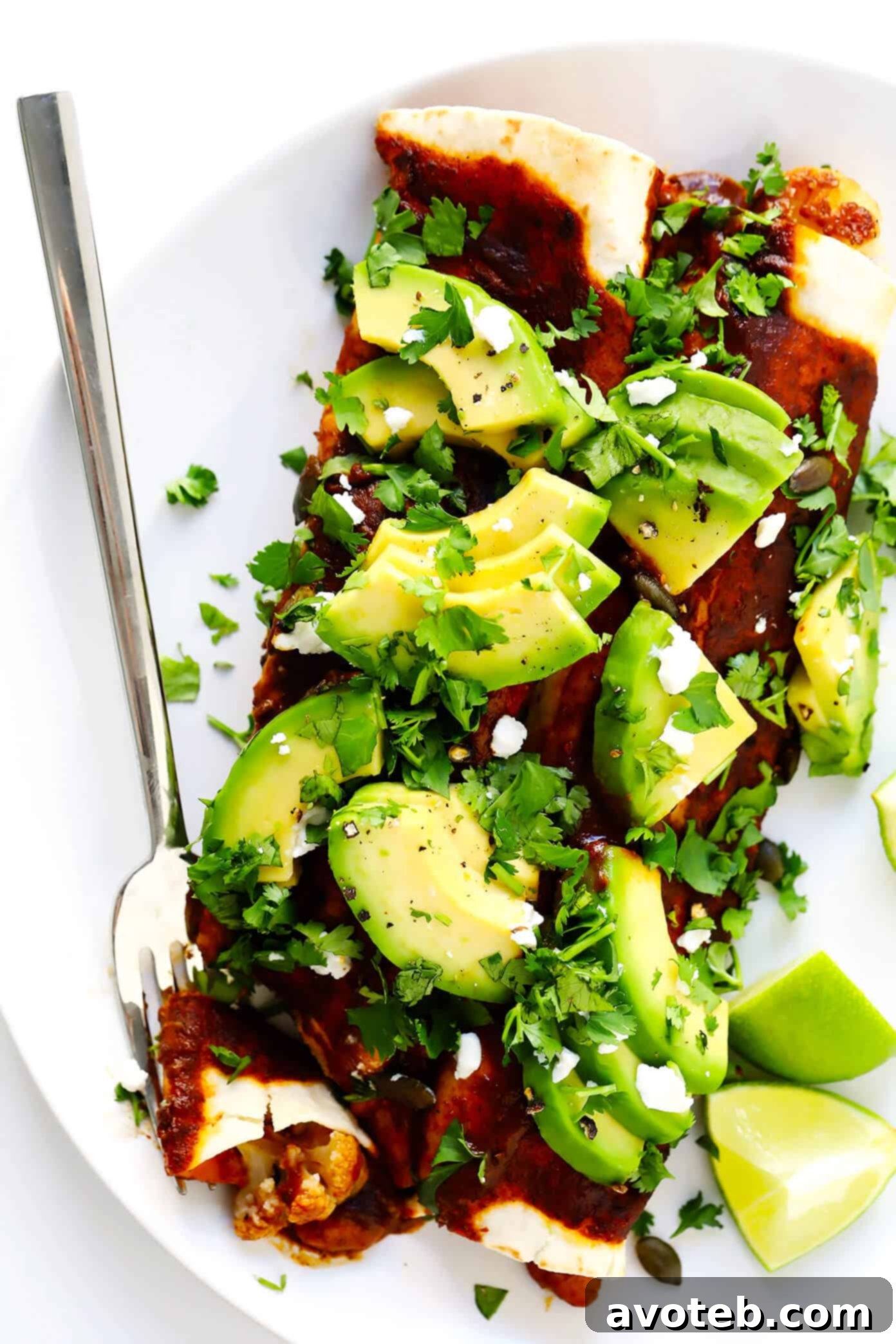 A wider shot of a baking dish filled with Vegetarian Roasted Cauliflower Enchiladas, garnished with avocado and cilantro, ready to be served.