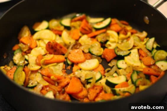 Close-up of sweet potatoes, zucchini, and onion cooking in a pan