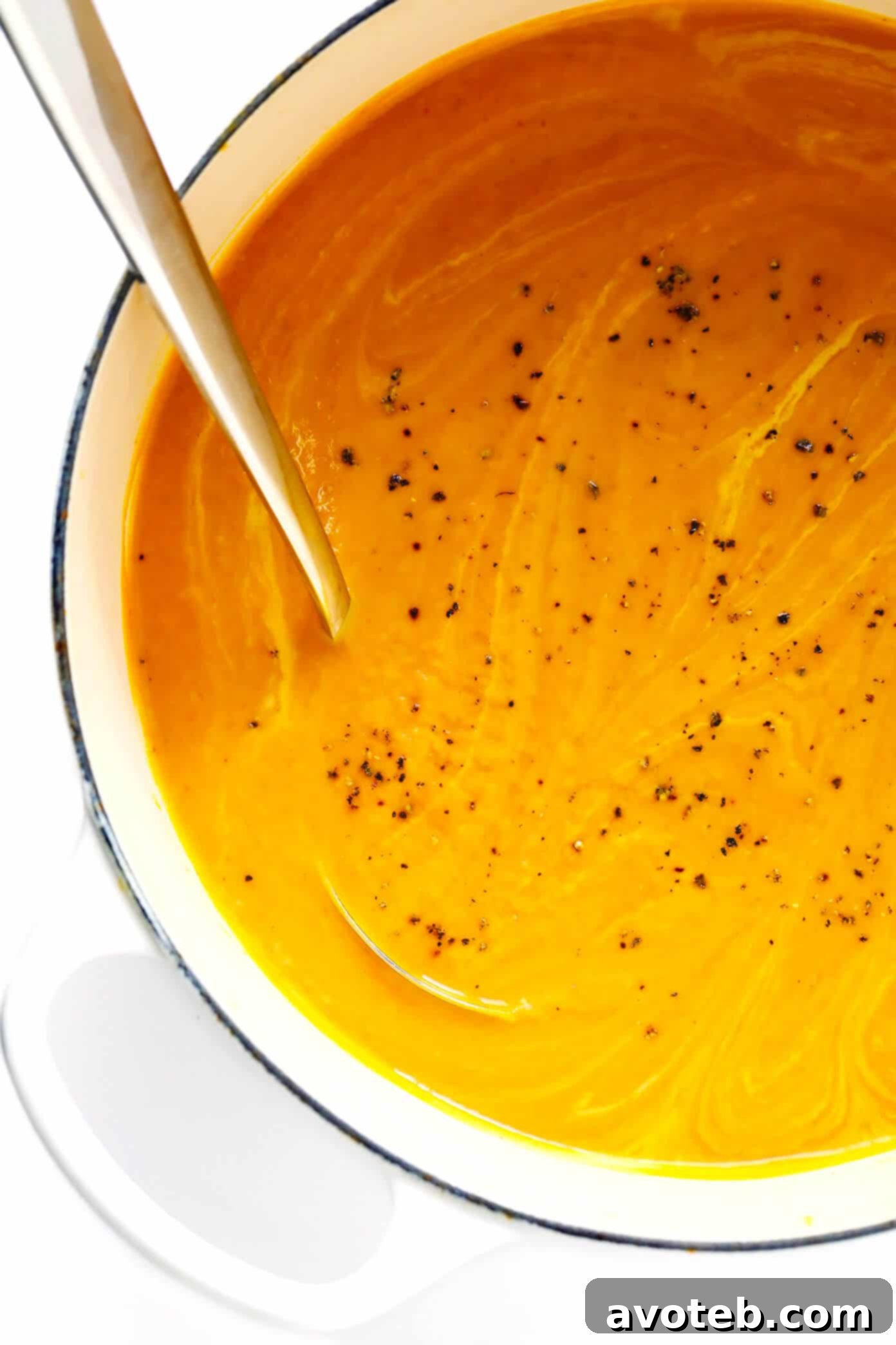 A bowl of vibrant Thai Curried Pumpkin Soup, topped with fresh cilantro, pepitas, and a lime wedge. The rich, creamy texture is visible.