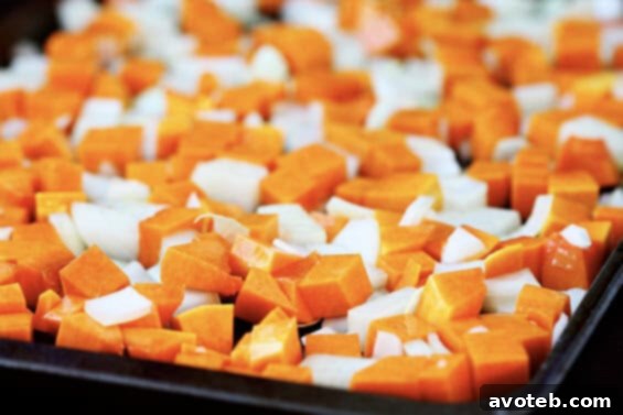 Butternut squash cubes and sliced yellow onion ready for roasting, seasoned and dotted with butter, on a baking sheet.