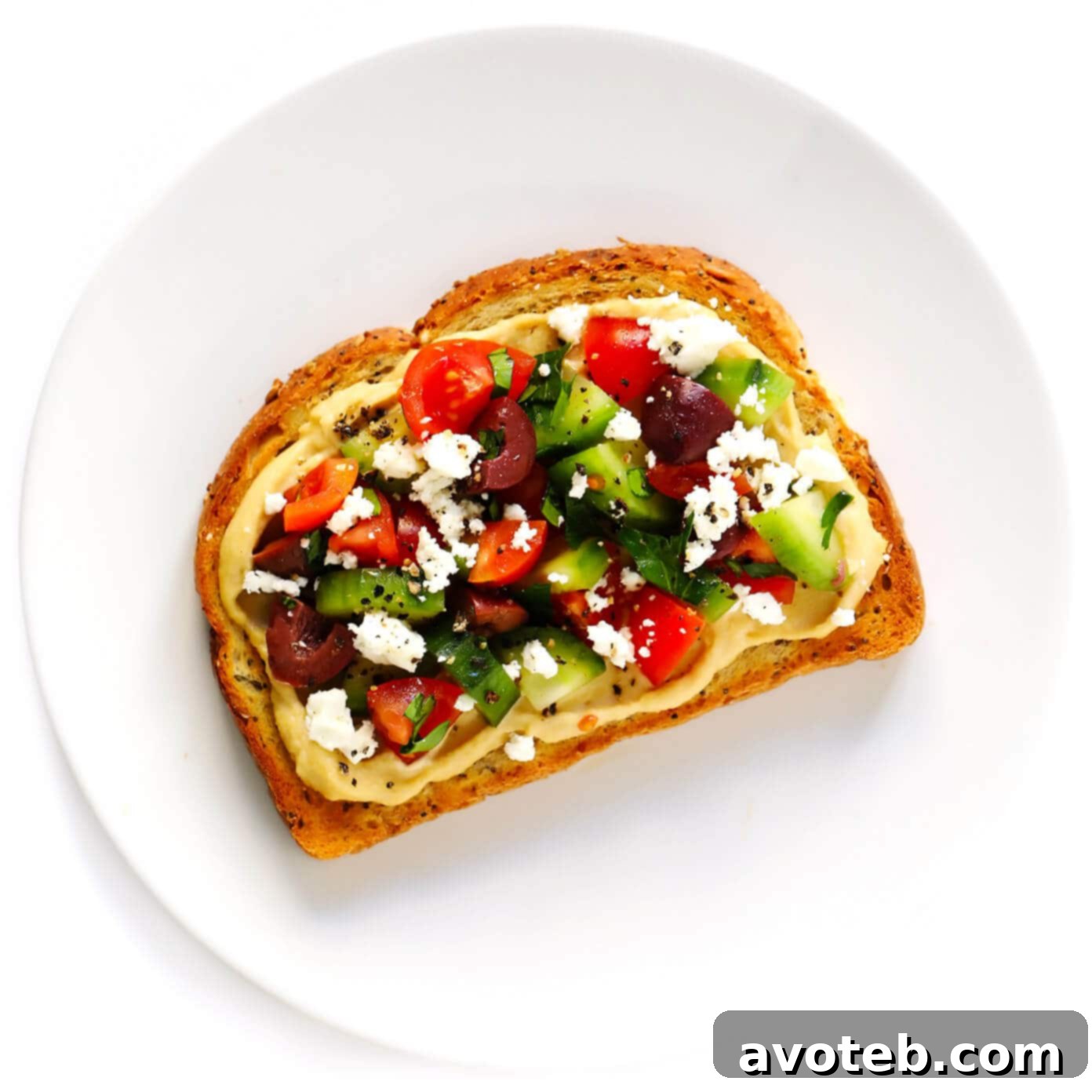 Hummus Toast featuring a colorful medley of chopped cucumber, tomatoes, olives, feta cheese, and parsley.