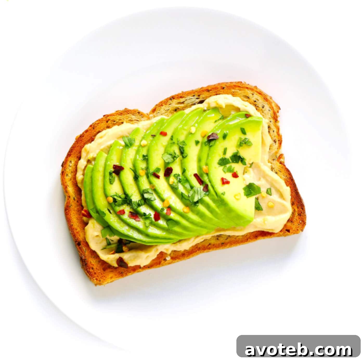 Hummus Toast topped with creamy avocado slices, cilantro, and chili flakes.