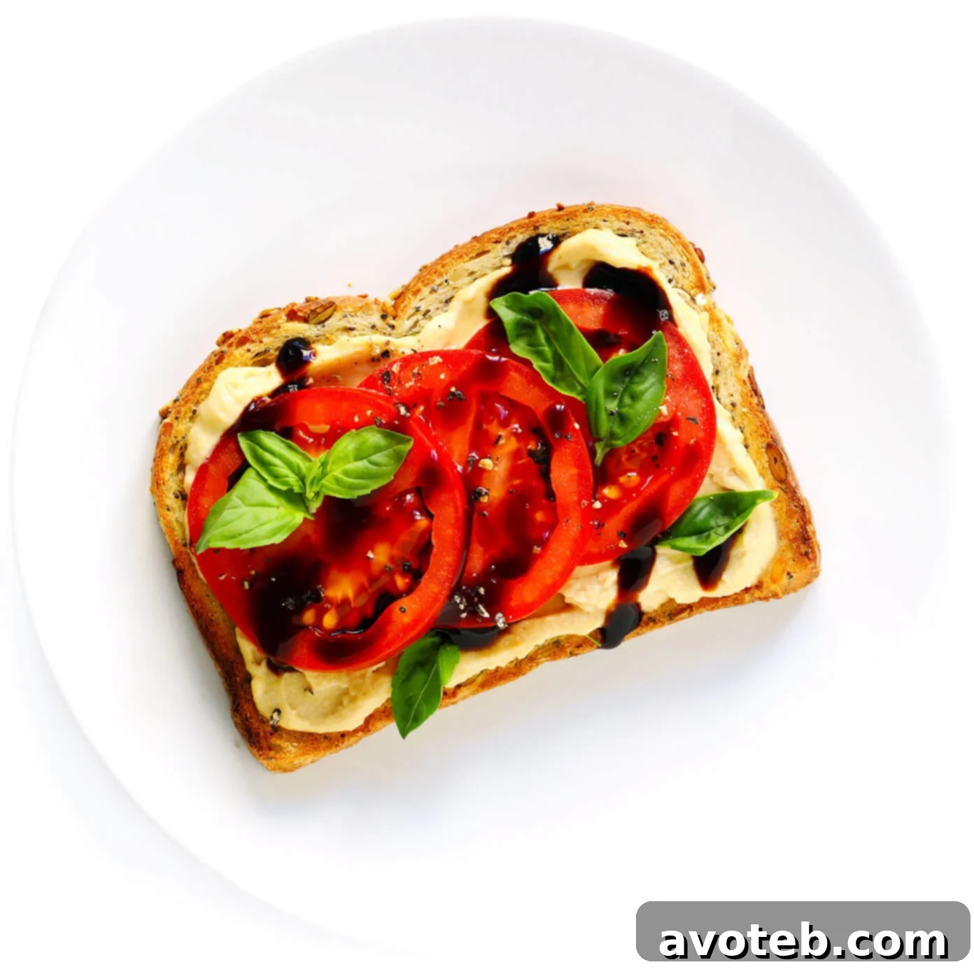 Hummus Toast adorned with fresh tomato slices, basil leaves, and a drizzle of balsamic glaze.
