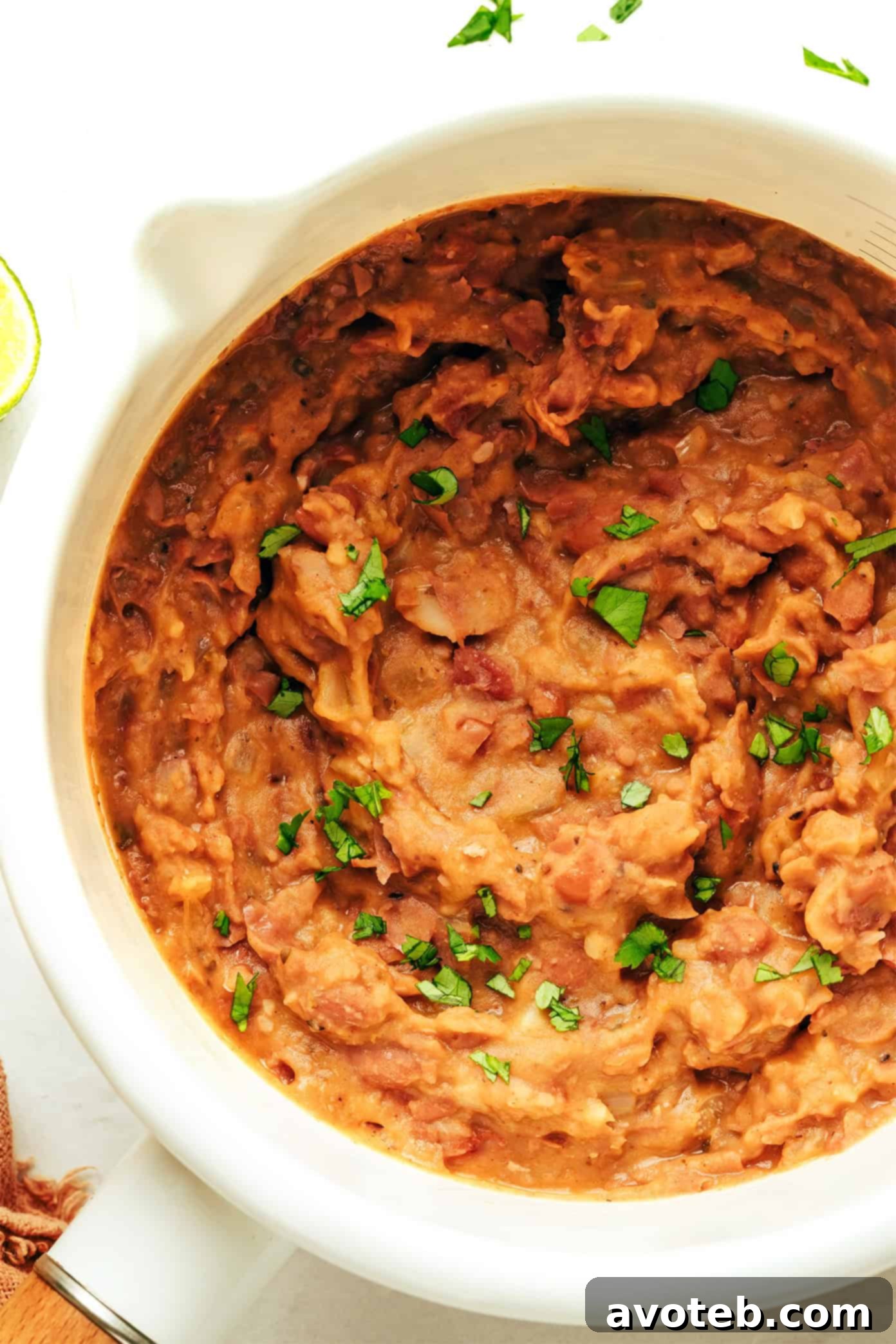 A delicious bowl of homemade refried beans, garnished with fresh cilantro and lime wedges, showcasing their inviting texture.