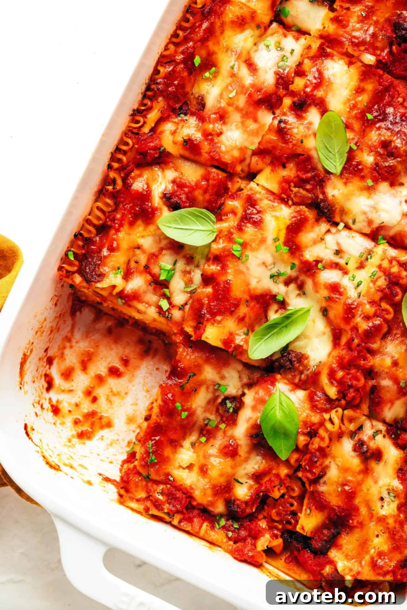 A beautifully layered and baked lasagna, garnished with fresh basil, ready to be served from a white baking dish.