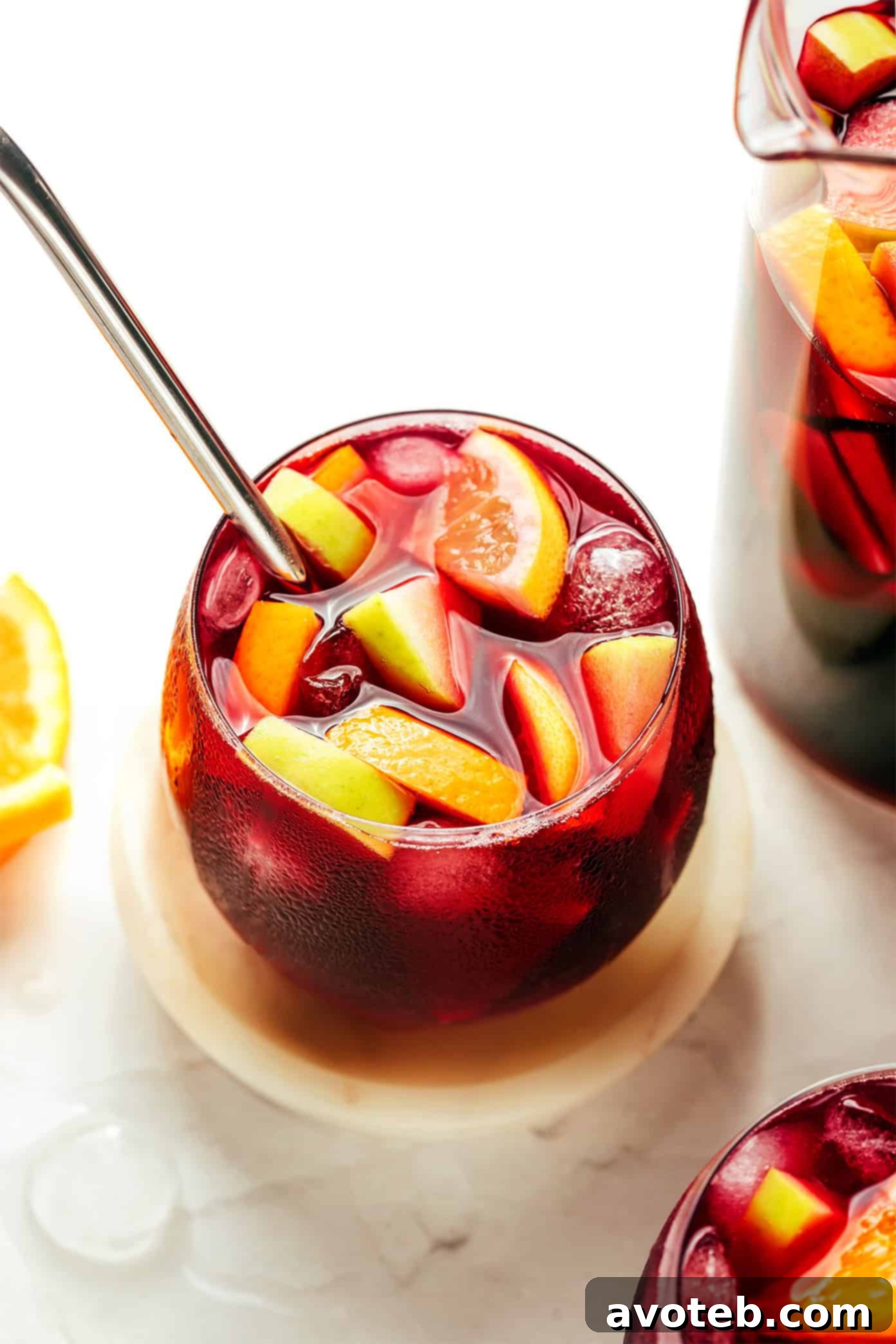 A beautifully garnished pitcher of red sangria, showcasing fresh fruit slices and a cinnamon stick, ready to be served over ice.