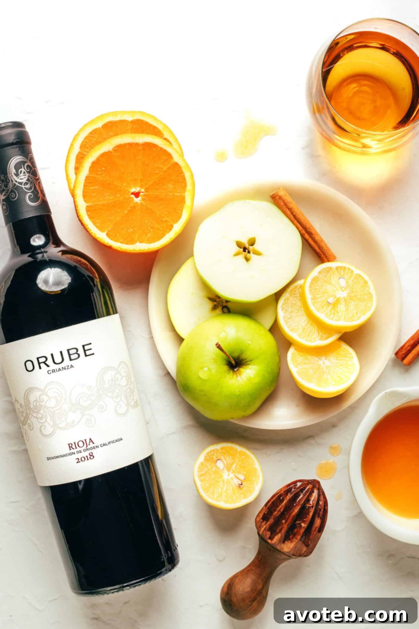 A close-up shot of a glass of sangria with ice, brimming with sliced oranges, lemons, and green apples, against a backdrop of a full pitcher.