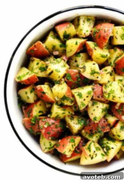 A bowl of vibrant French Potato Salad, garnished with fresh herbs, against a light background.