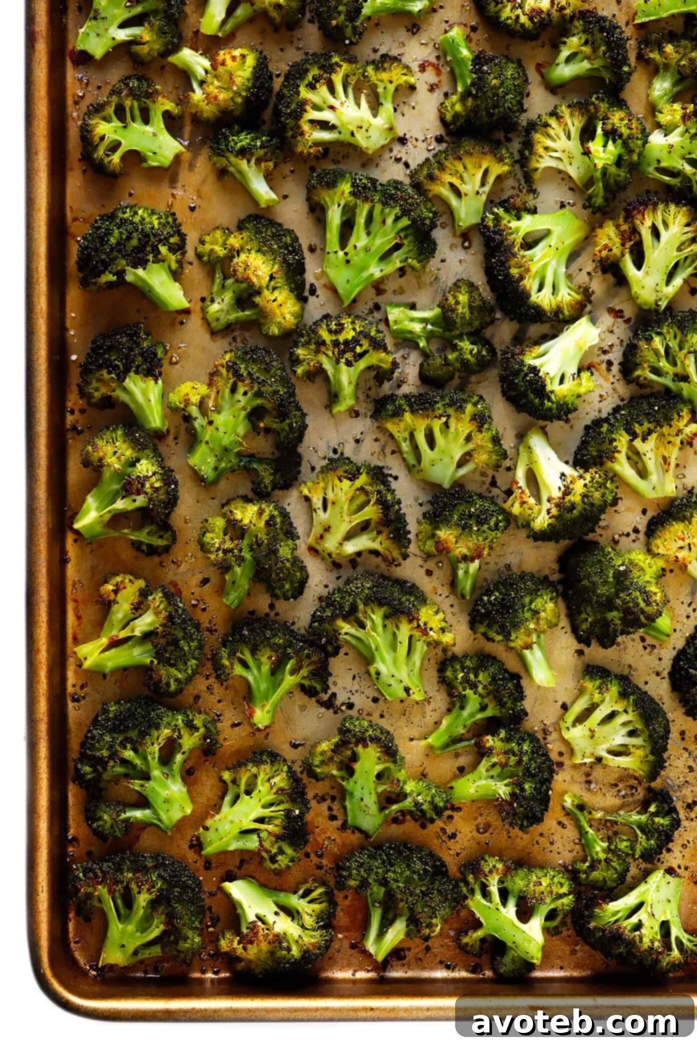 Hands tossing broccoli florets with olive oil, salt, and pepper on a baking sheet, preparing them for roasting.