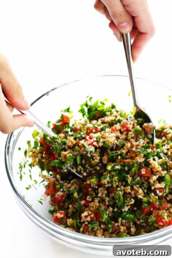 The process of mixing all the fresh ingredients for tabbouleh in a large bowl, ensuring even distribution of flavors.
