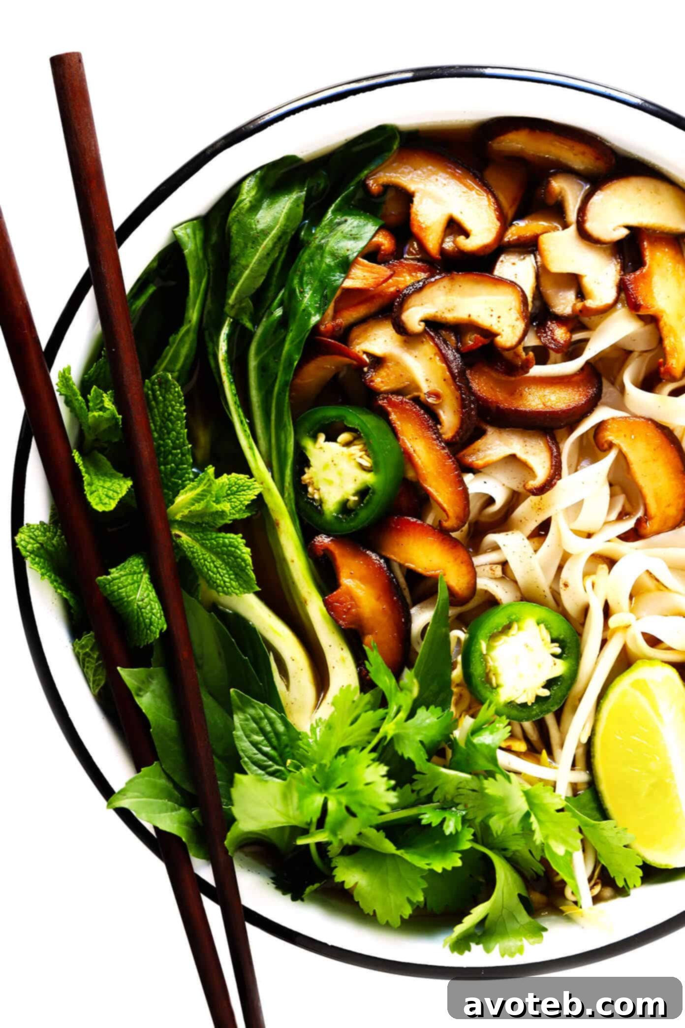 A bowl of vegan pho soup with rice noodles, vegetables, and fresh toppings