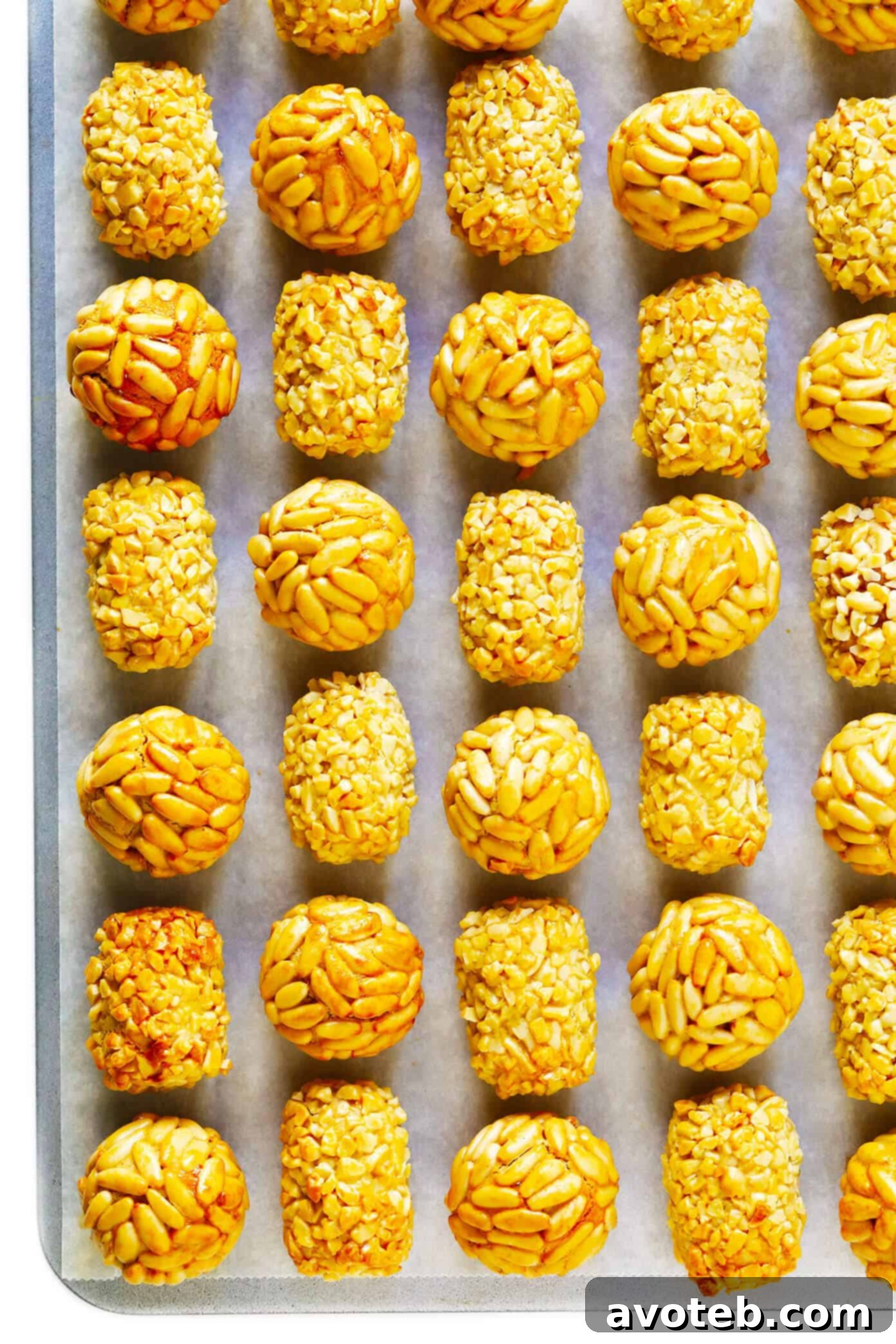 Two varieties of Panellets, one covered in golden pine nuts and another in finely chopped almonds, arranged on a rustic wooden surface.
