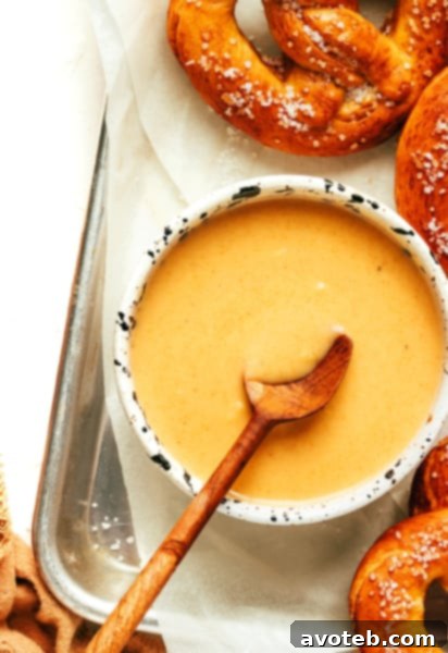 A bowl of creamy beer cheese dip with pretzel bites, beer bottles, and cheese slices around it.