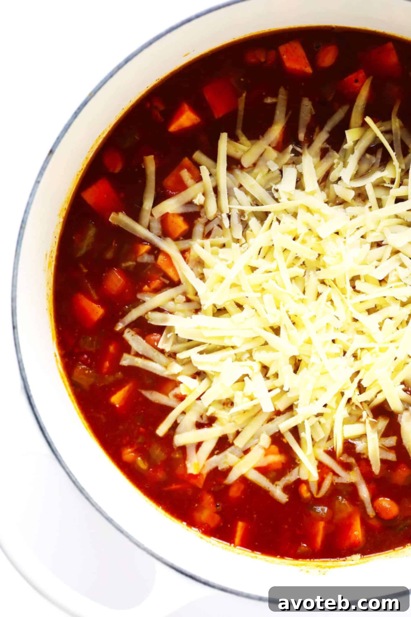 Rich and creamy cheesy sweet potato enchilada soup garnished with avocado and cilantro, in a white bowl.