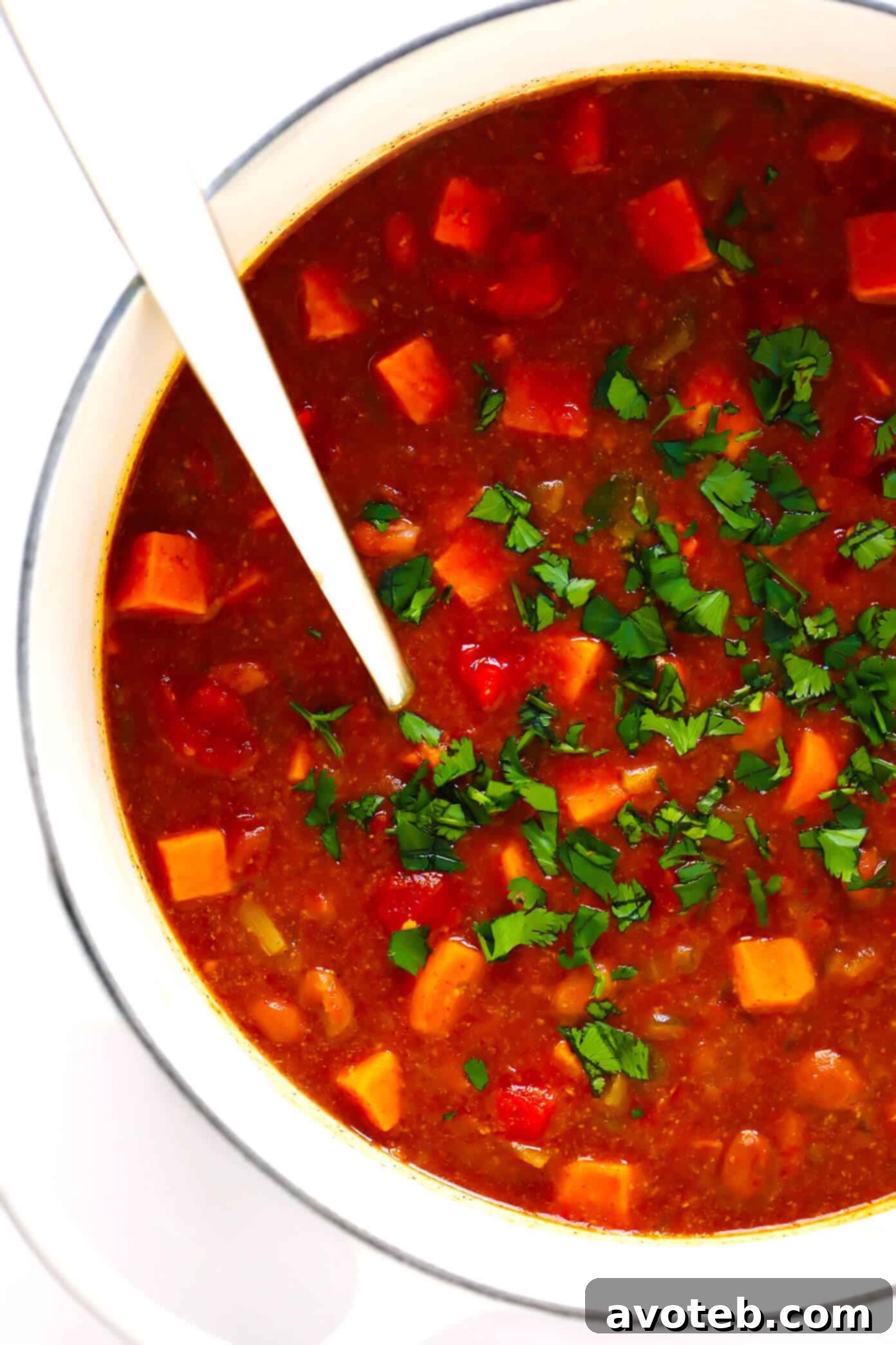A bowl of vibrant vegetarian sweet potato chili, topped with fresh avocado, cilantro, and crumbled tortilla chips.