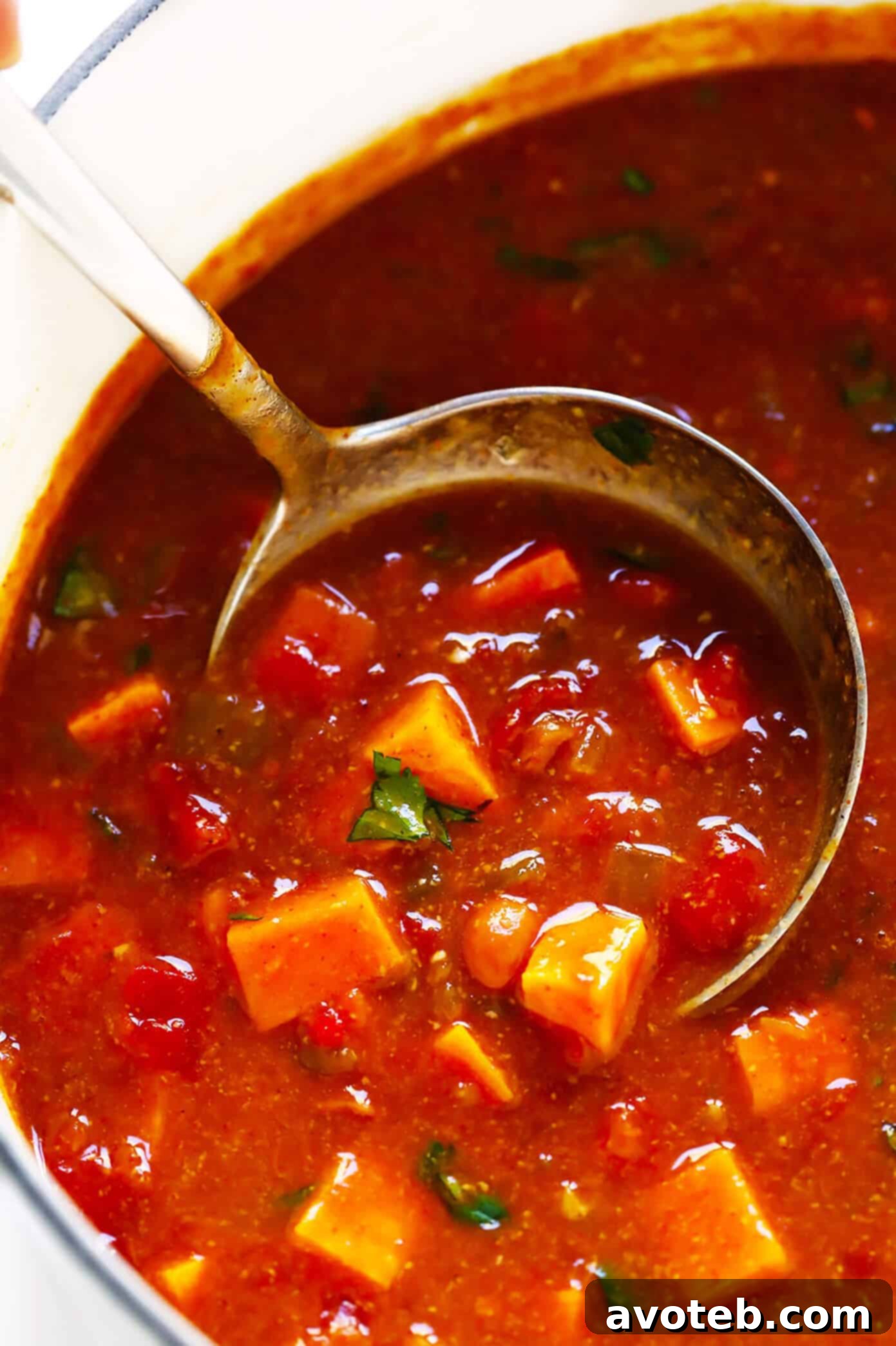 A beautifully composed shot of Sweet Potato Enchilada Soup in a bowl, with avocado, cilantro, and a lime wedge.