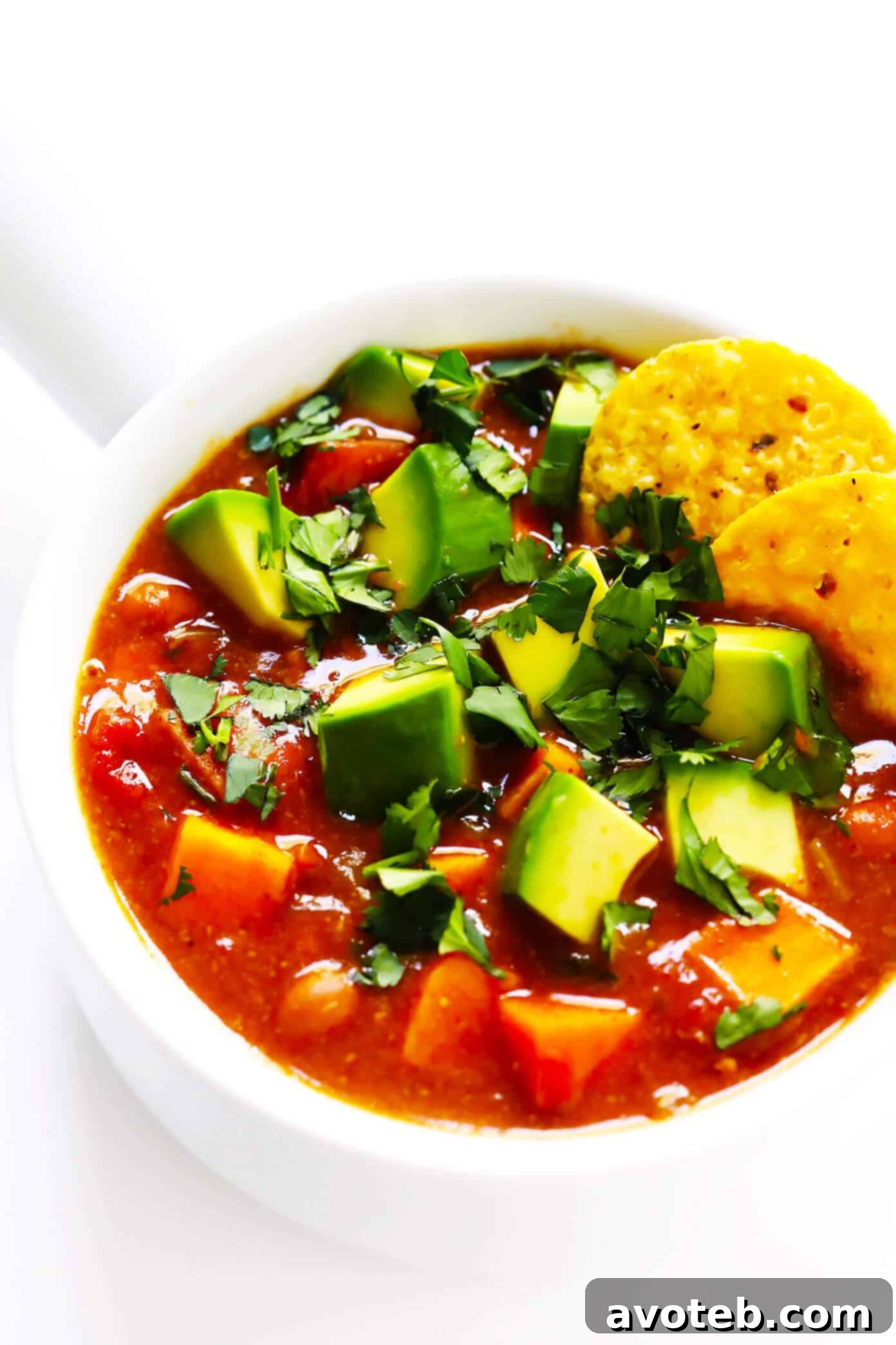 A close-up shot of a rustic bowl filled with sweet potato chili, topped with fresh green onion and cheese.