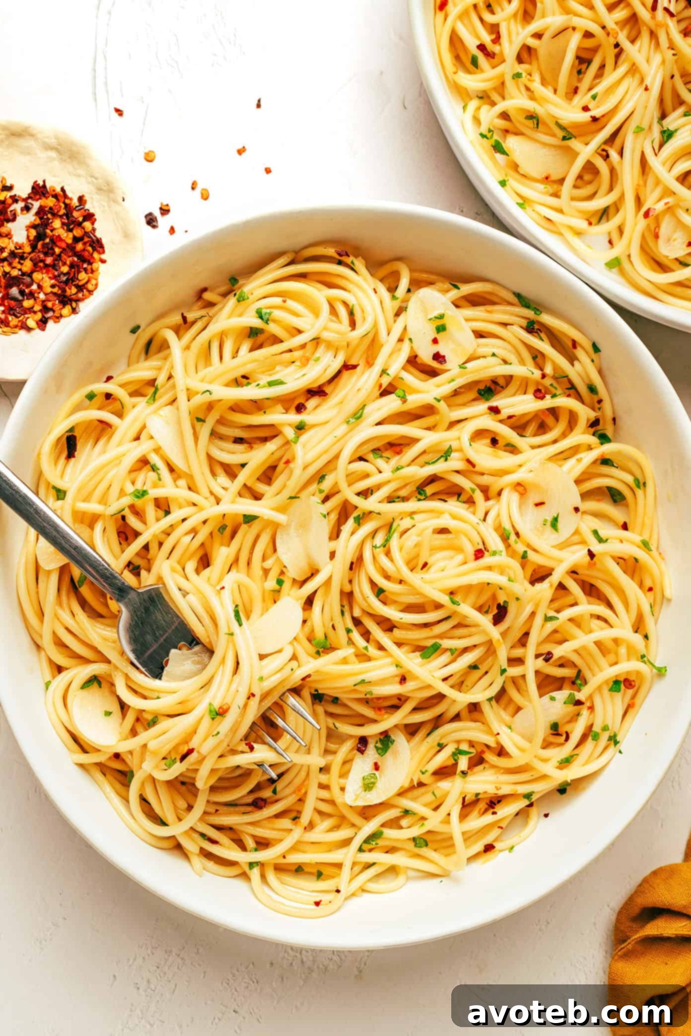 A full bowl of Spaghetti Aglio e Olio, generously garnished with fresh parsley and grated Parmesan cheese.