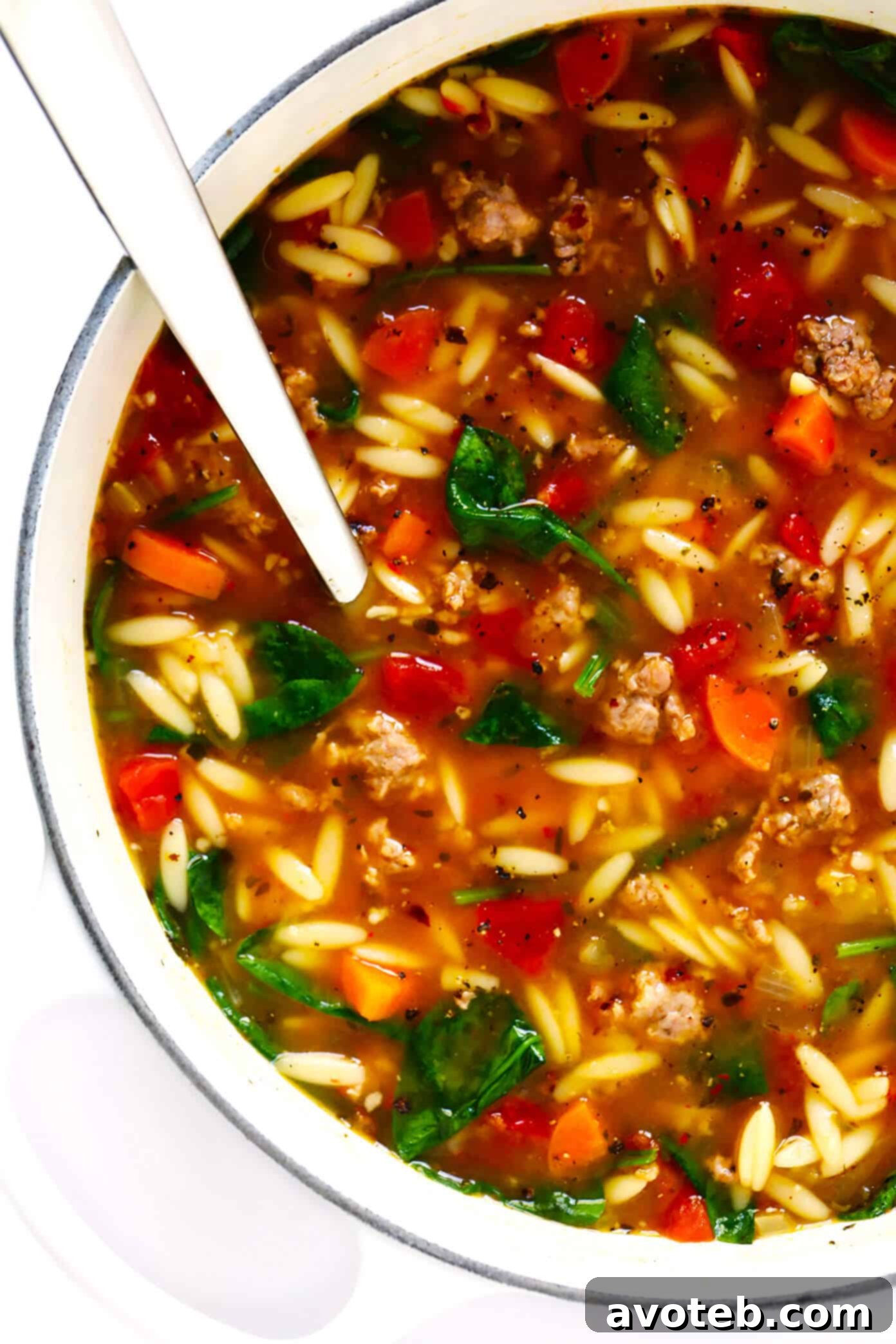 Italian Soup with Sausage, Orzo and Spinach - A close-up shot of a steaming bowl of Italian soup, showcasing crumbled sausage, golden orzo, and wilted spinach in a rich tomato broth.