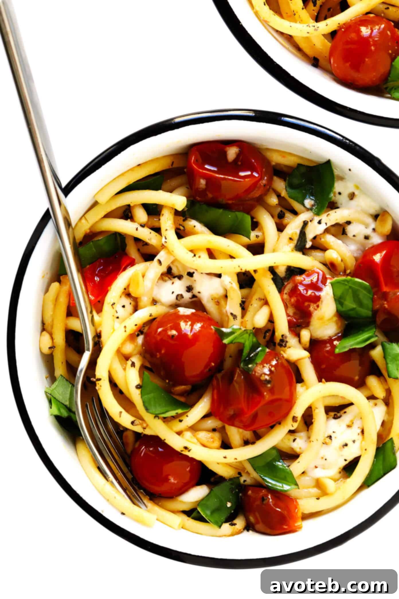 A vibrant bowl of garlicky pasta with burst cherry tomatoes, melting burrata cheese, and fresh basil leaves, garnished with toasted pine nuts, ready to be served.