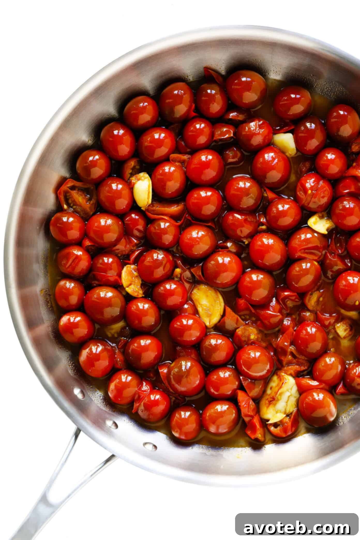 Close-up shot of a rich, bubbly sauce made from burst cherry tomatoes and garlic simmering in a pan, forming the base for a delicious pasta dish.
