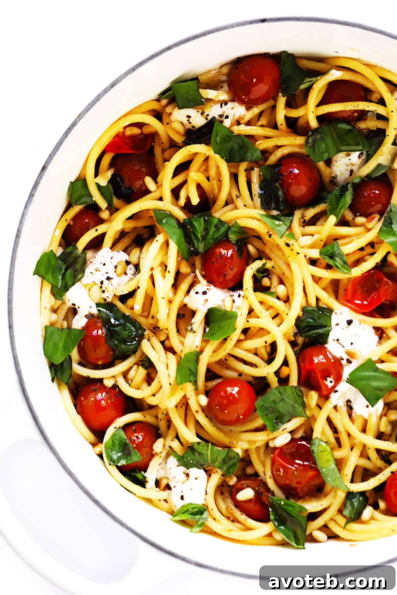 A large pot of bucatini pasta mixed with creamy burrata cheese, vibrant burst cherry tomatoes, fresh basil leaves, and toasted pine nuts, creating a rich and inviting meal.