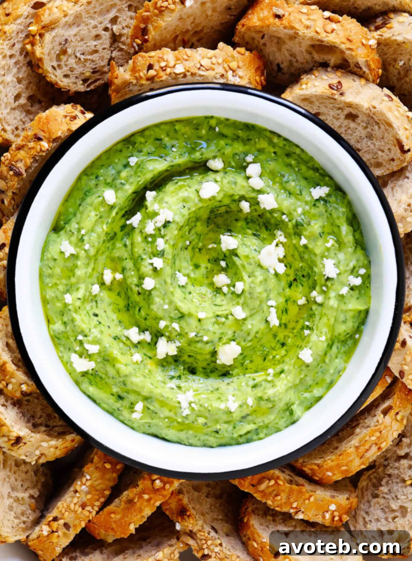 An inviting bowl of Green Goddess Feta Dip, artfully garnished, surrounded by slices of warm, crusty bread, ready for dipping.