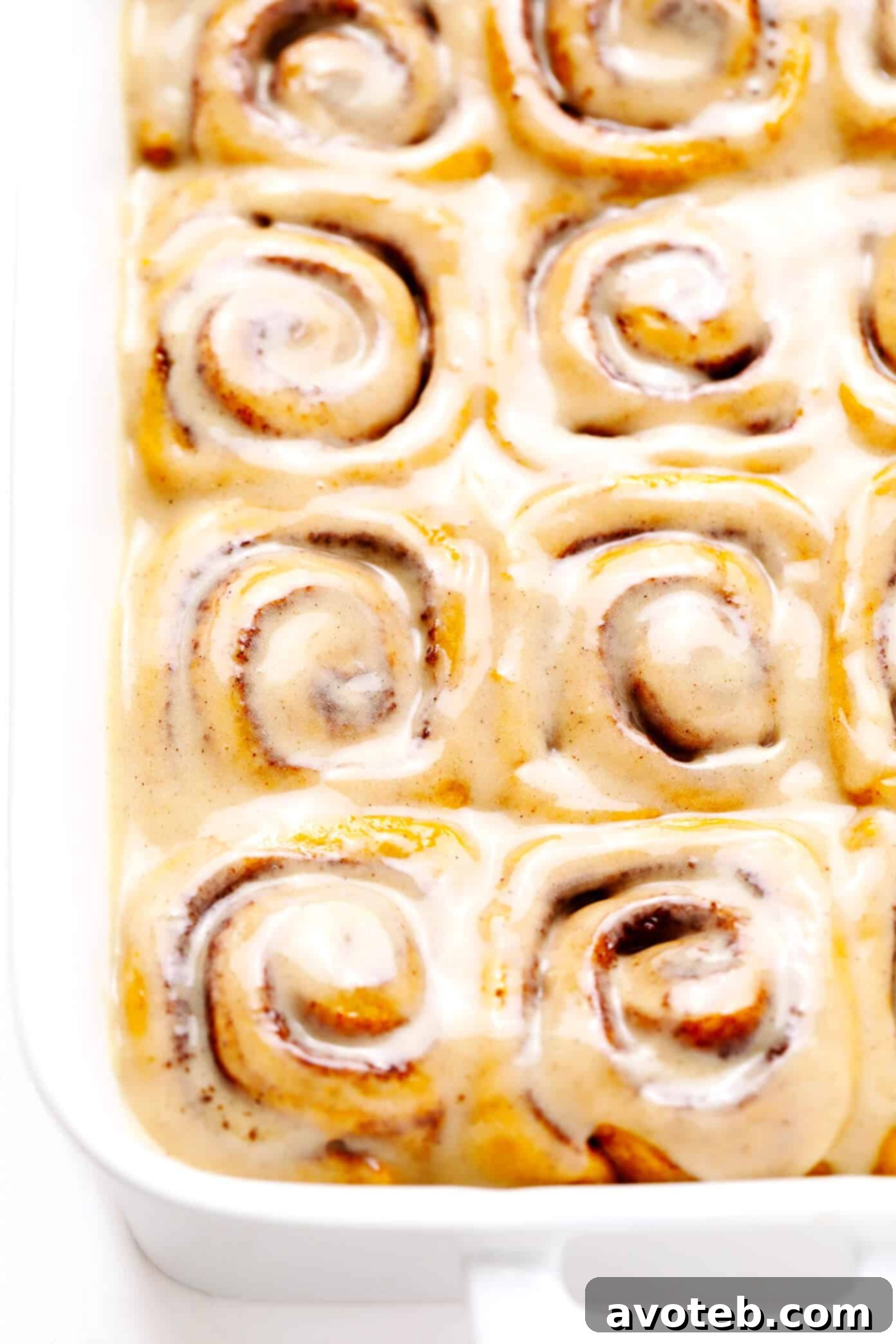 A baking pan filled with freshly baked Pumpkin Cinnamon Rolls, still warm from the oven, awaiting their generous topping of creamy maple frosting.