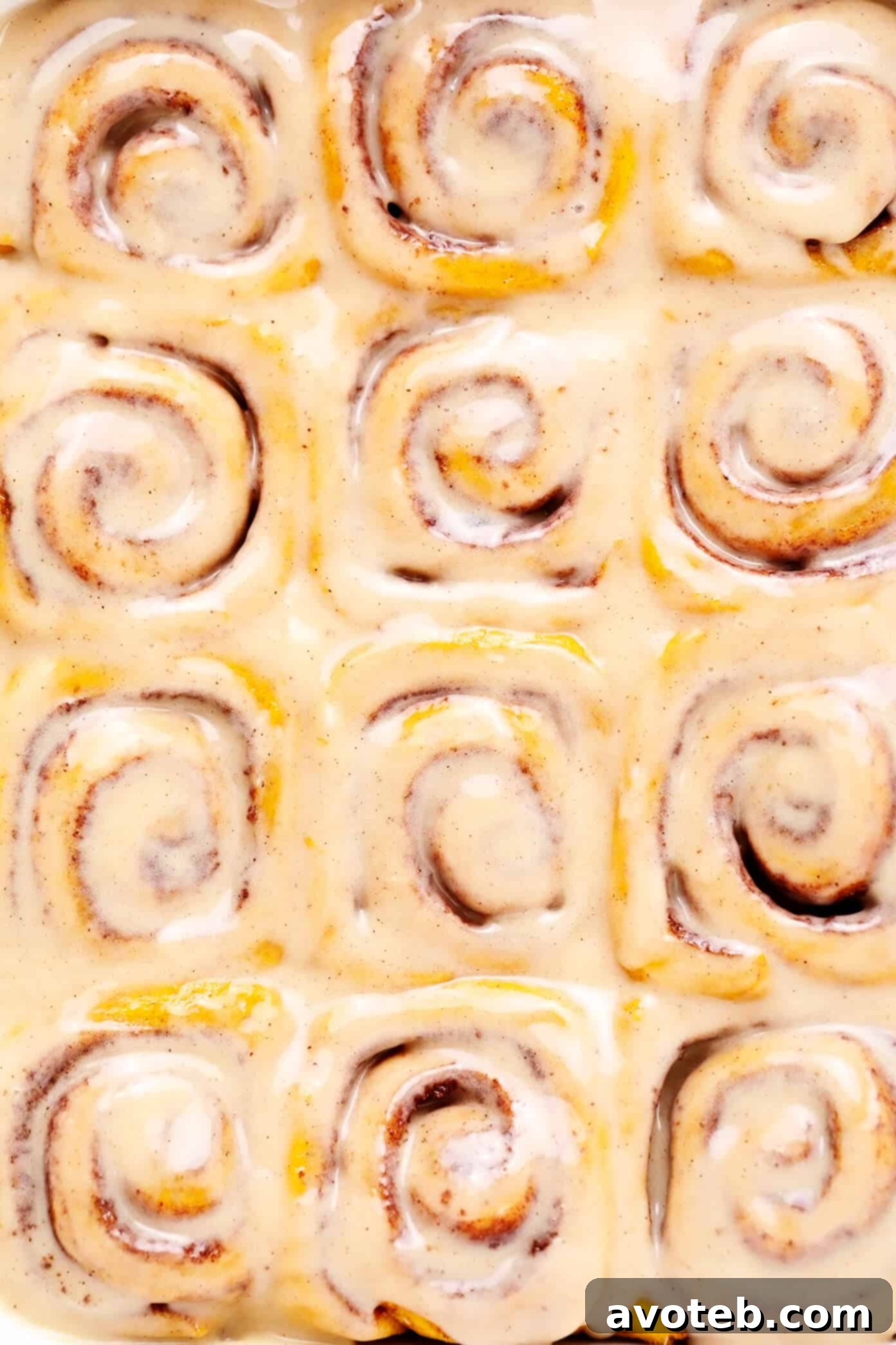 A mesmerizing close-up of freshly baked Pumpkin Cinnamon Rolls, showcasing their soft interior, golden edges, and generously applied maple cream cheese frosting.