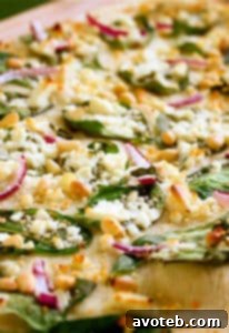 Spinach Feta and Pine Nut Pizza with a golden crust, ready to be sliced