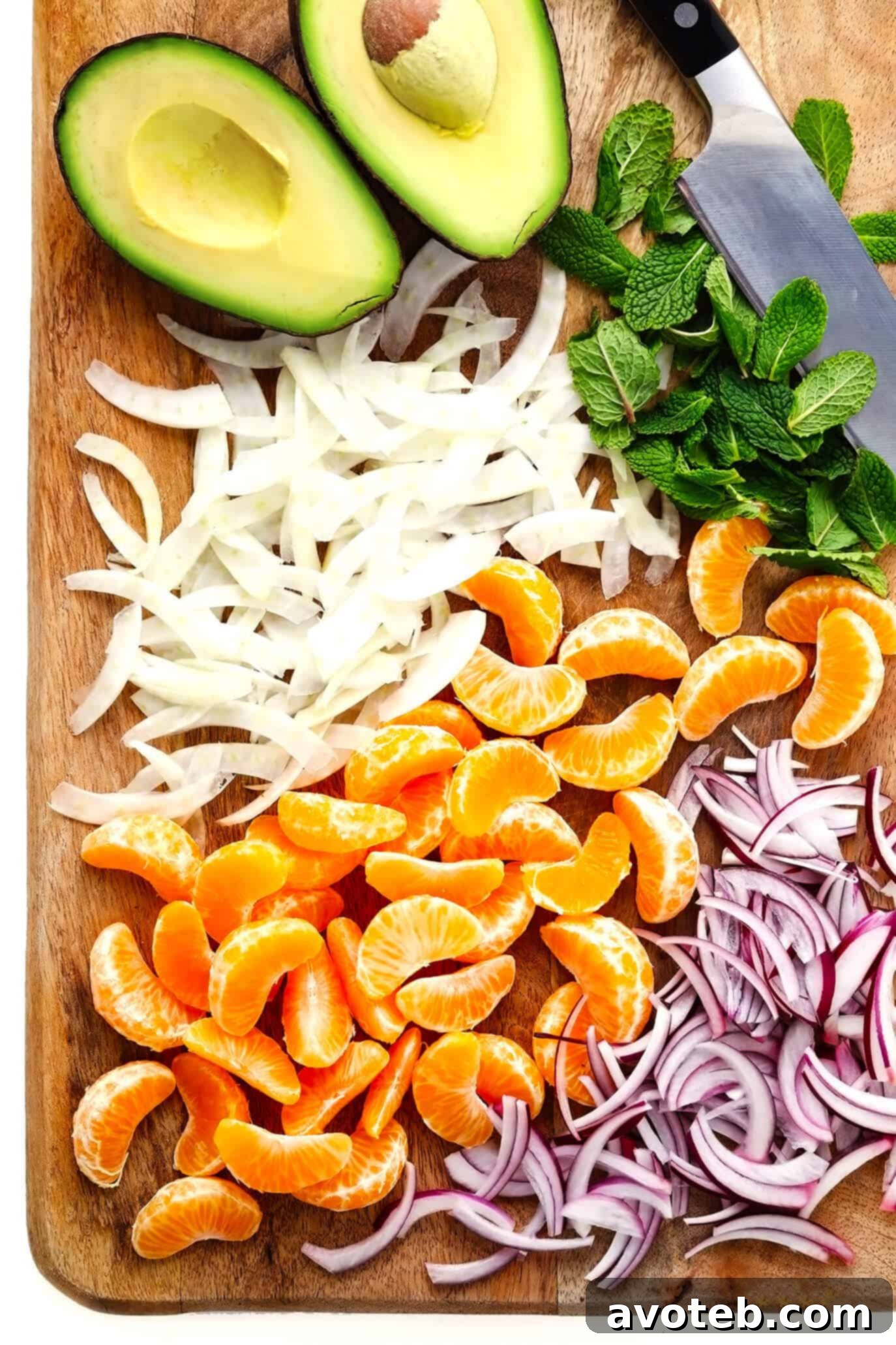 Cutting board with fresh avocado, fennel, red onion, mint and clementine oranges, prepped for salad.