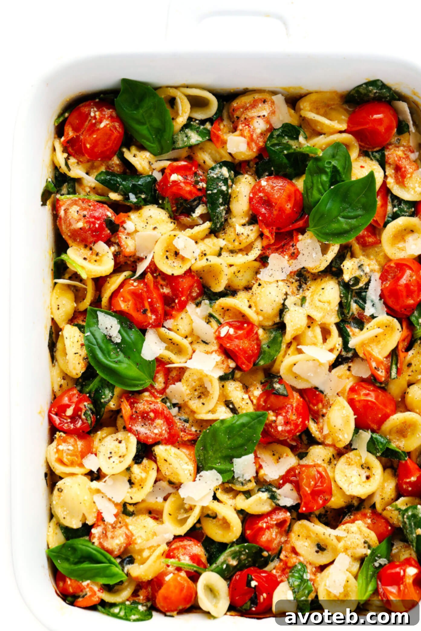 My spin on TikTok's famous baked feta pasta recipe is super-easy to make in the oven, featuring creamy melted feta cheese, burst cherry tomatoes, fresh spinach, and the yummiest garlic white wine basil sauce. Feel free to add a protein (chicken, shrimp, salmon, etc) or extra veggies too, and you're welcome to use gluten-free pasta to make this recipe gf. | gimmesomeoven.com #pasta #feta #cheese #vegetarian #dinner #easy #uunifetapasta #tomato #sauce TikTok Feta Pasta recipe baking in a dish, with feta and tomatoes.