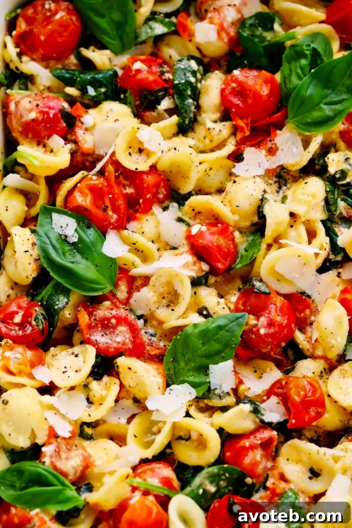 My spin on TikTok's famous baked feta pasta recipe is super-easy to make in the oven, featuring creamy melted feta cheese, burst cherry tomatoes, fresh spinach, and the yummiest garlic white wine basil sauce. Feel free to add a protein (chicken, shrimp, salmon, etc) or extra veggies too, and you're welcome to use gluten-free pasta to make this recipe gf. | gimmesomeoven.com #pasta #feta #cheese #vegetarian #dinner #easy #uunifetapasta #tomato #sauce Baked Feta Pasta Recipe Closeup, showing creamy sauce and fresh basil.