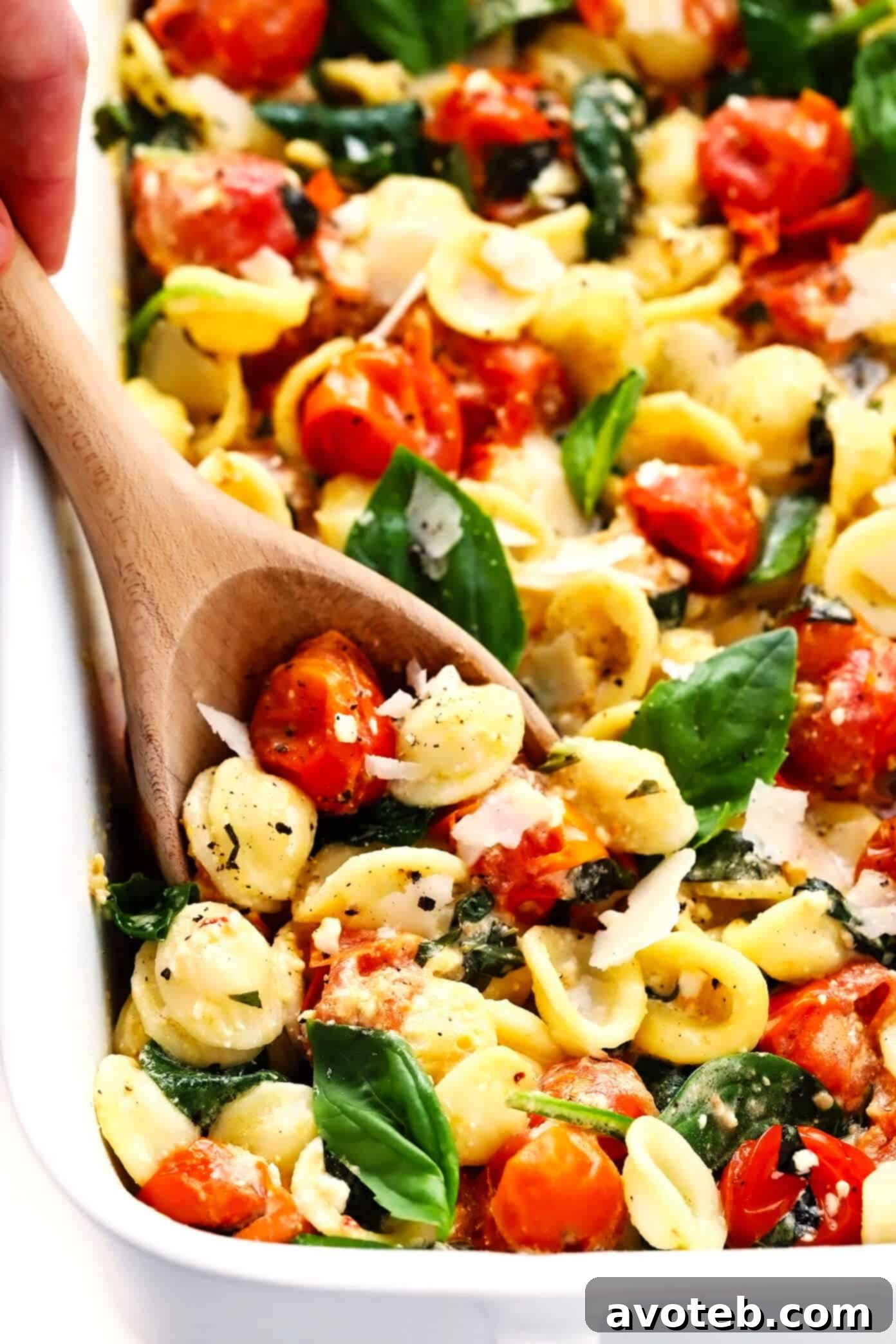 My spin on TikTok's famous baked feta pasta recipe is super-easy to make in the oven, featuring creamy melted feta cheese, burst cherry tomatoes, fresh spinach, and the yummiest garlic white wine basil sauce. Feel free to add a protein (chicken, shrimp, salmon, etc) or extra veggies too, and you're welcome to use gluten-free pasta to make this recipe gf. | gimmesomeoven.com #pasta #feta #cheese #vegetarian #dinner #easy #uunifetapasta #tomato #sauce Baked Feta Pasta Recipe with Serving Spoon, showing generous portions.