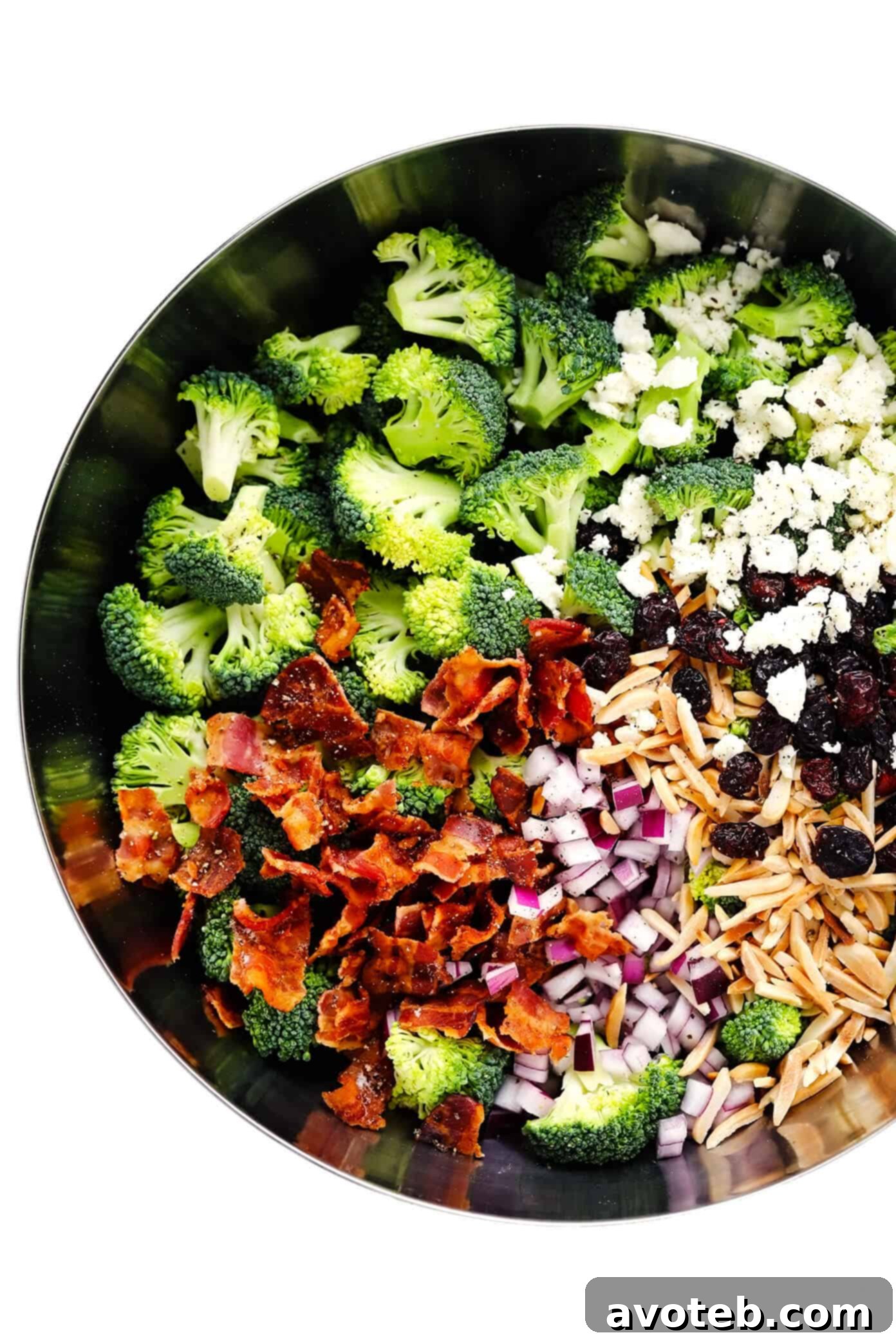 Broccoli Salad Ingredients in a bowl: Fresh Broccoli Florets, Crispy Bacon, Red Onion, Toasted Almonds, Dried Cranberries, and Feta Cheese