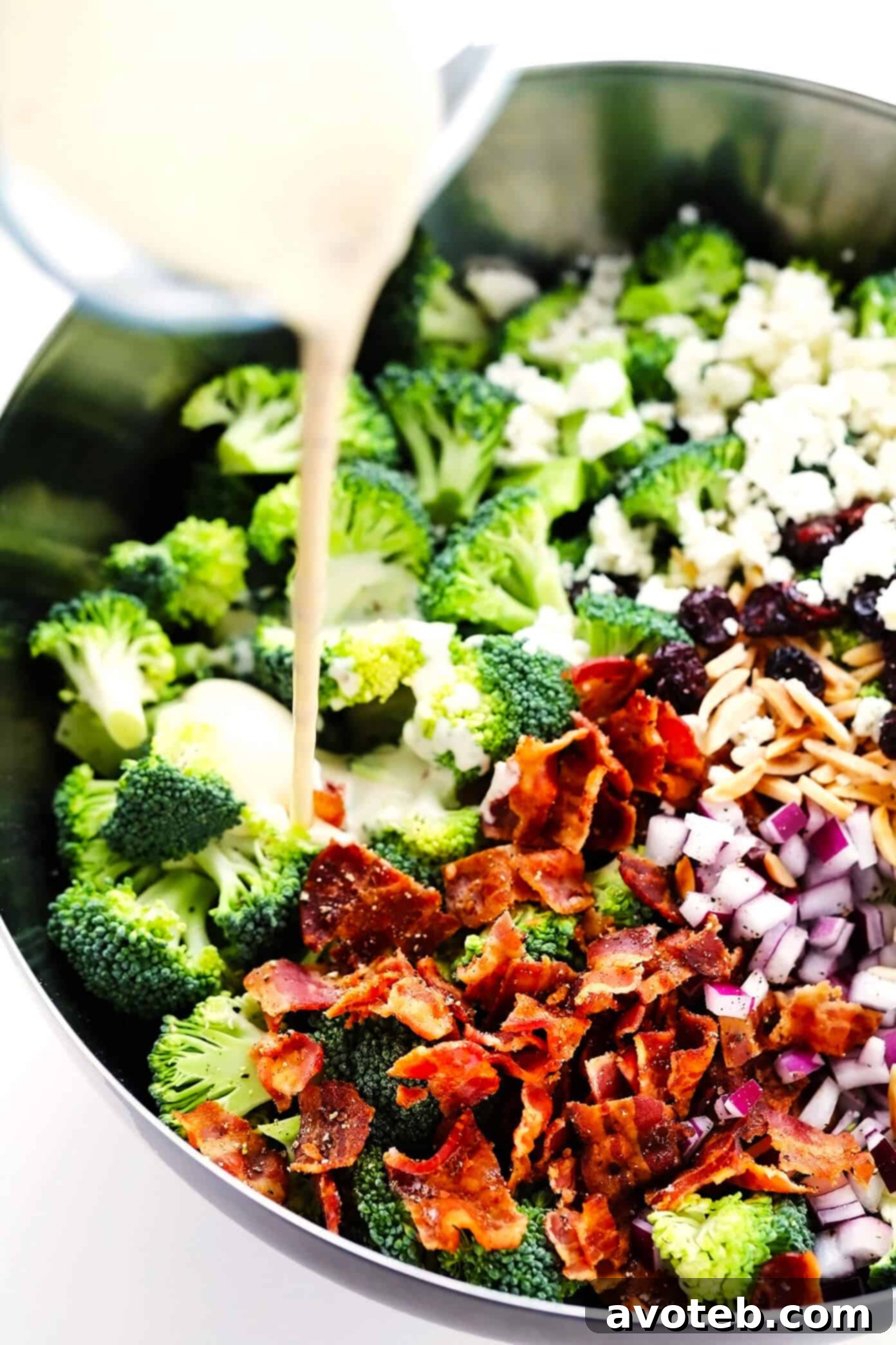 Pouring creamy dressing over the broccoli salad ingredients in a mixing bowl