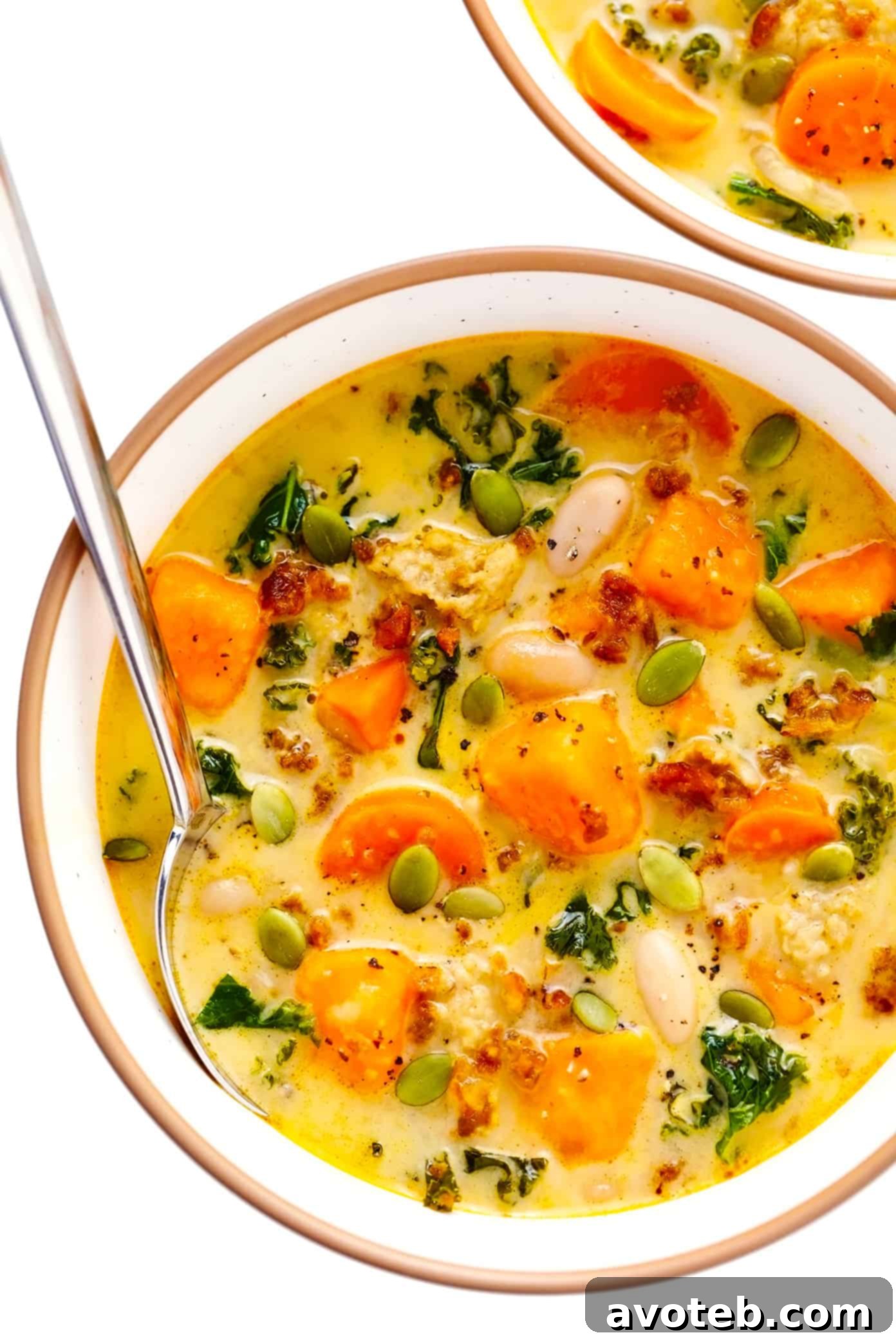 A beautiful serving bowl filled with creamy sweet potato and sausage soup, garnished and ready to enjoy. | gimmesomeoven.com Serving bowl of creamy sweet potato and sausage soup with white beans and kale