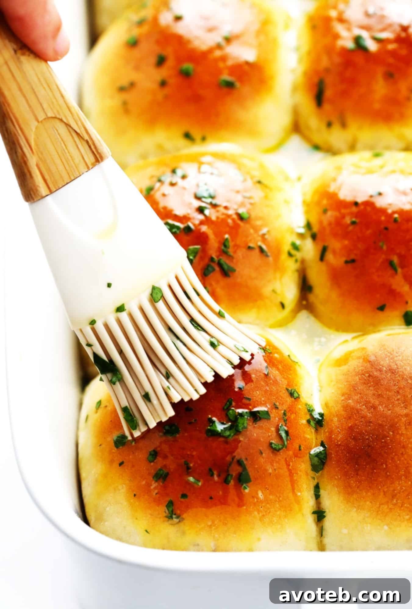 Brushing dinner rolls with garlic butter - A hand gracefully brushes golden-brown rosemary garlic dinner rolls with a melted garlic herb butter, enhancing their flavor and shine.