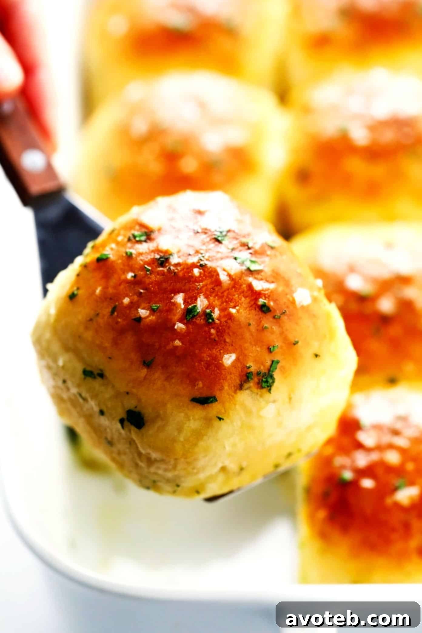 Rosemary Garlic Dinner Rolls Closeup - An extreme close-up of a single rosemary garlic dinner roll, showcasing its soft, fluffy texture, golden crust, and visible flecks of fresh herbs and garlic.