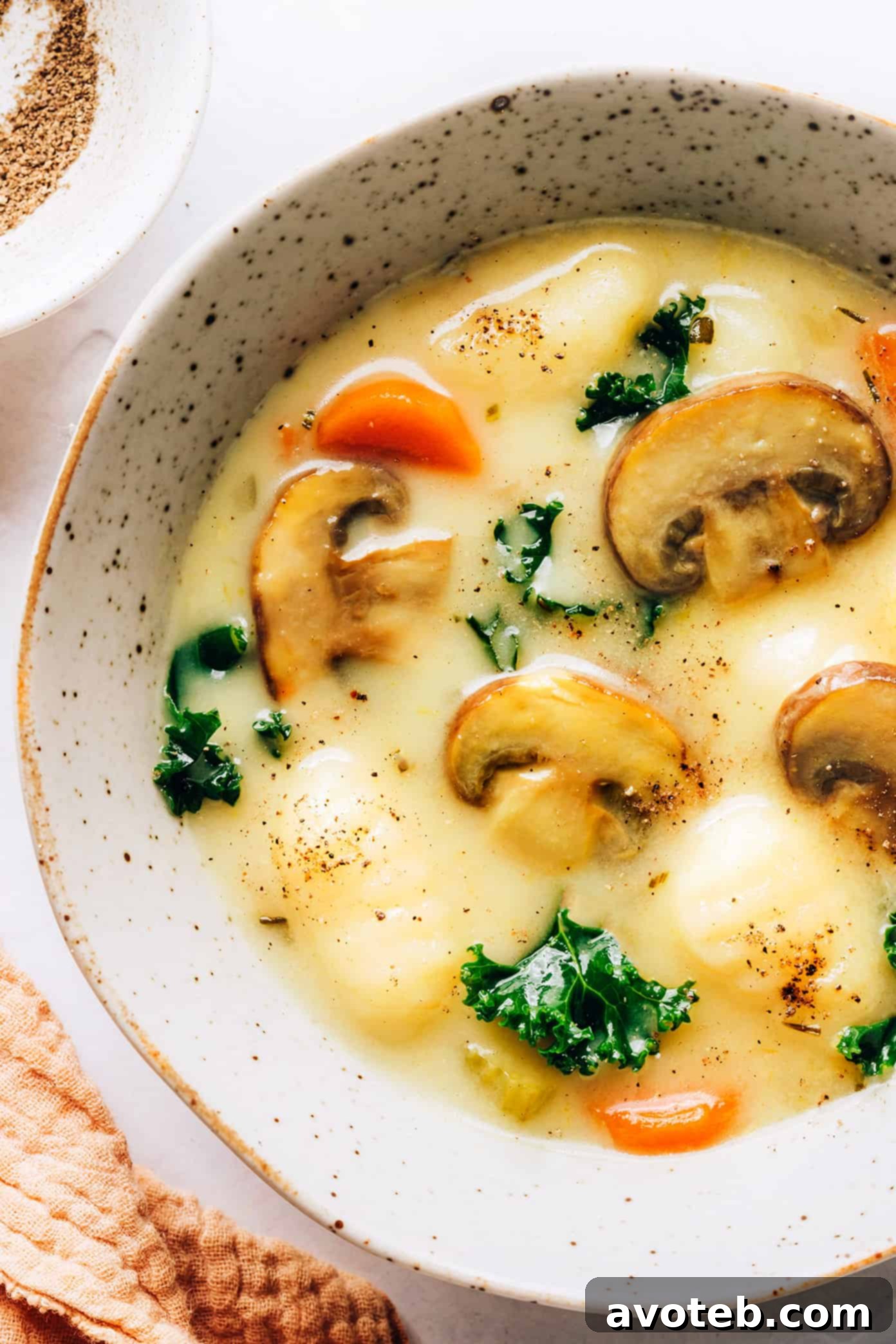 A mouth-watering close-up of the creamy Gnocchi, Mushroom, and Kale Soup in a bowl, showing the rich broth, tender gnocchi, and wilted kale, topped with Parmesan.