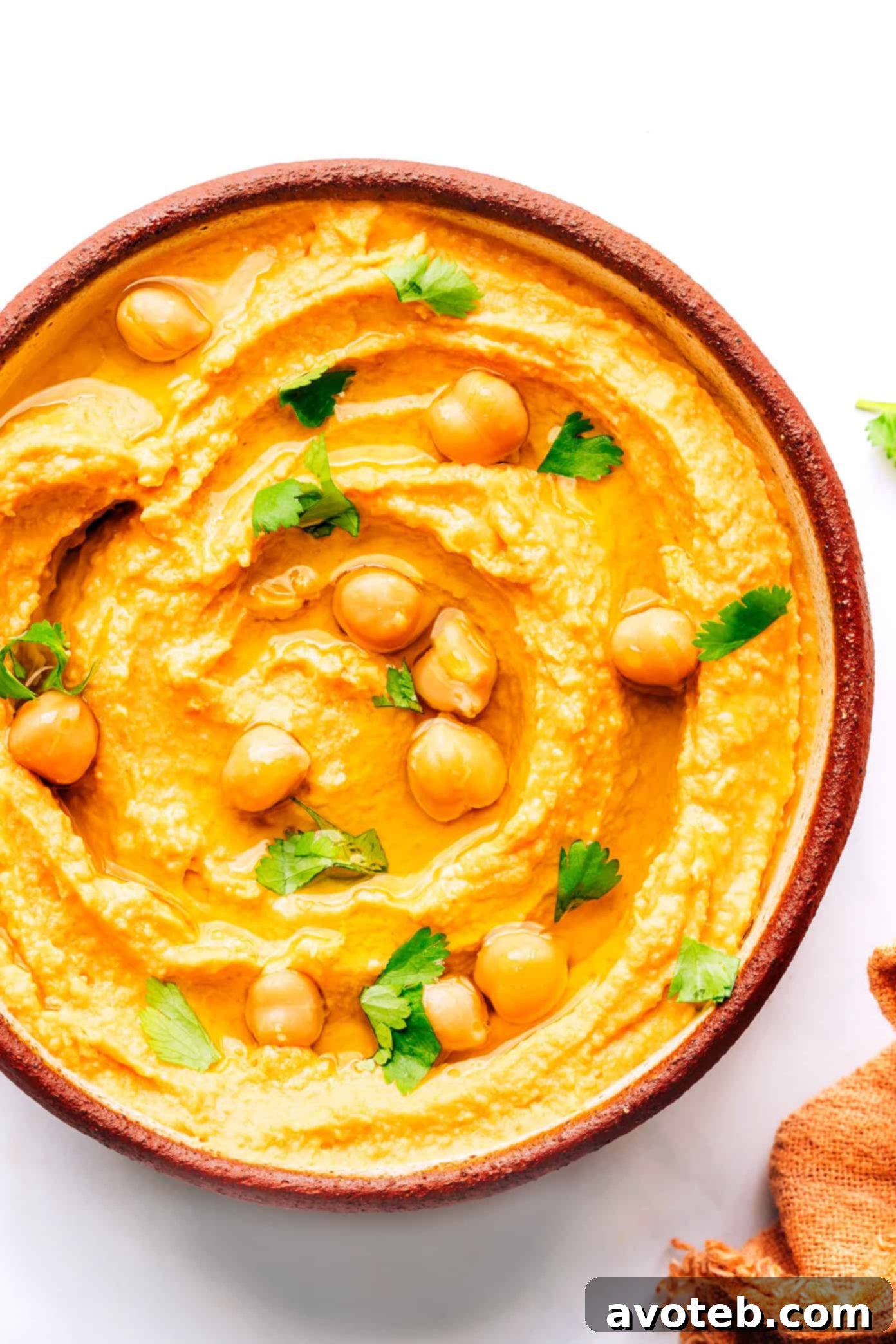 Thai Red Curry Hummus served in a white bowl, topped with whole chickpeas and fresh herbs, ready to be enjoyed.