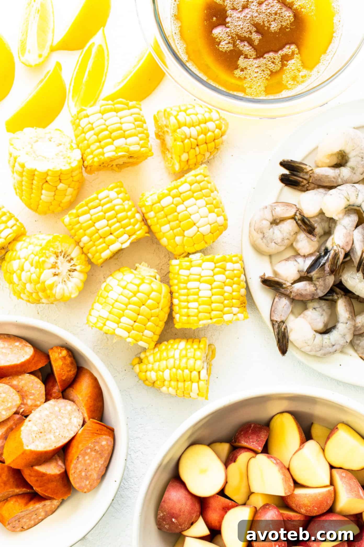 Ingredients for a classic shrimp boil: fresh lemons, corn on the cob, raw jumbo shrimp, Andouille sausage, red potatoes, and butter