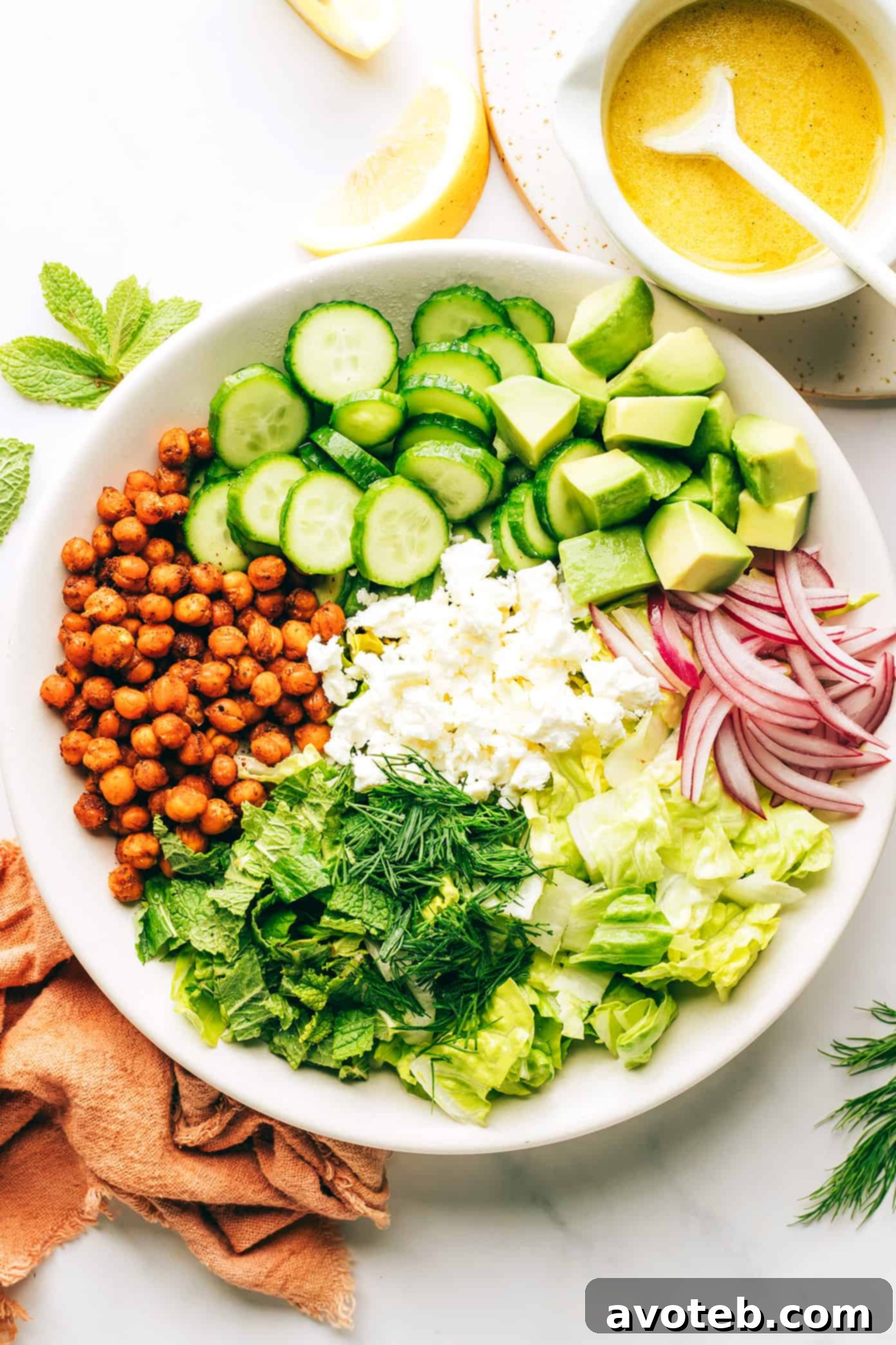 A close-up shot of the finished roasted chickpea, avocado, and cucumber salad, showing the vibrant colors, appealing textures, and fresh herb garnish in a white bowl.