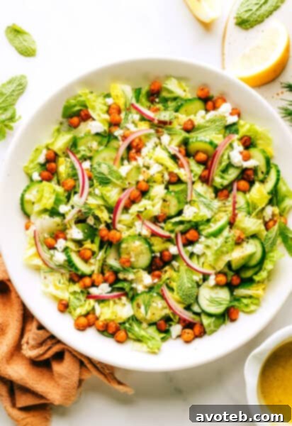 A vibrant bowl of roasted chickpea, avocado, and cucumber salad, garnished with fresh herbs, ready to be served.
