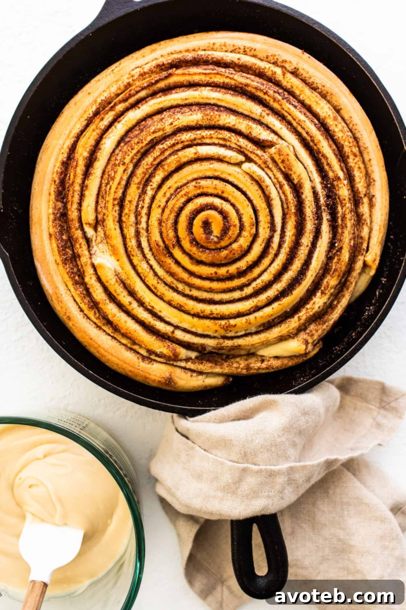 Unfrosted giant cinnamon roll baked to golden perfection in a cast iron skillet, waiting to be smothered in cream cheese frosting