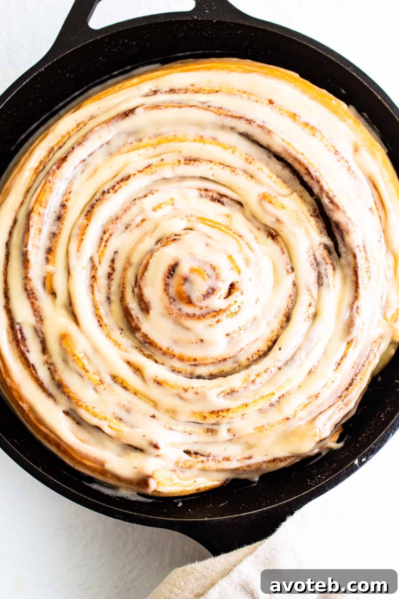 Giant Cinnamon Roll baked in a skillet, generously covered with a rich and tangy cream cheese icing, ready to be served