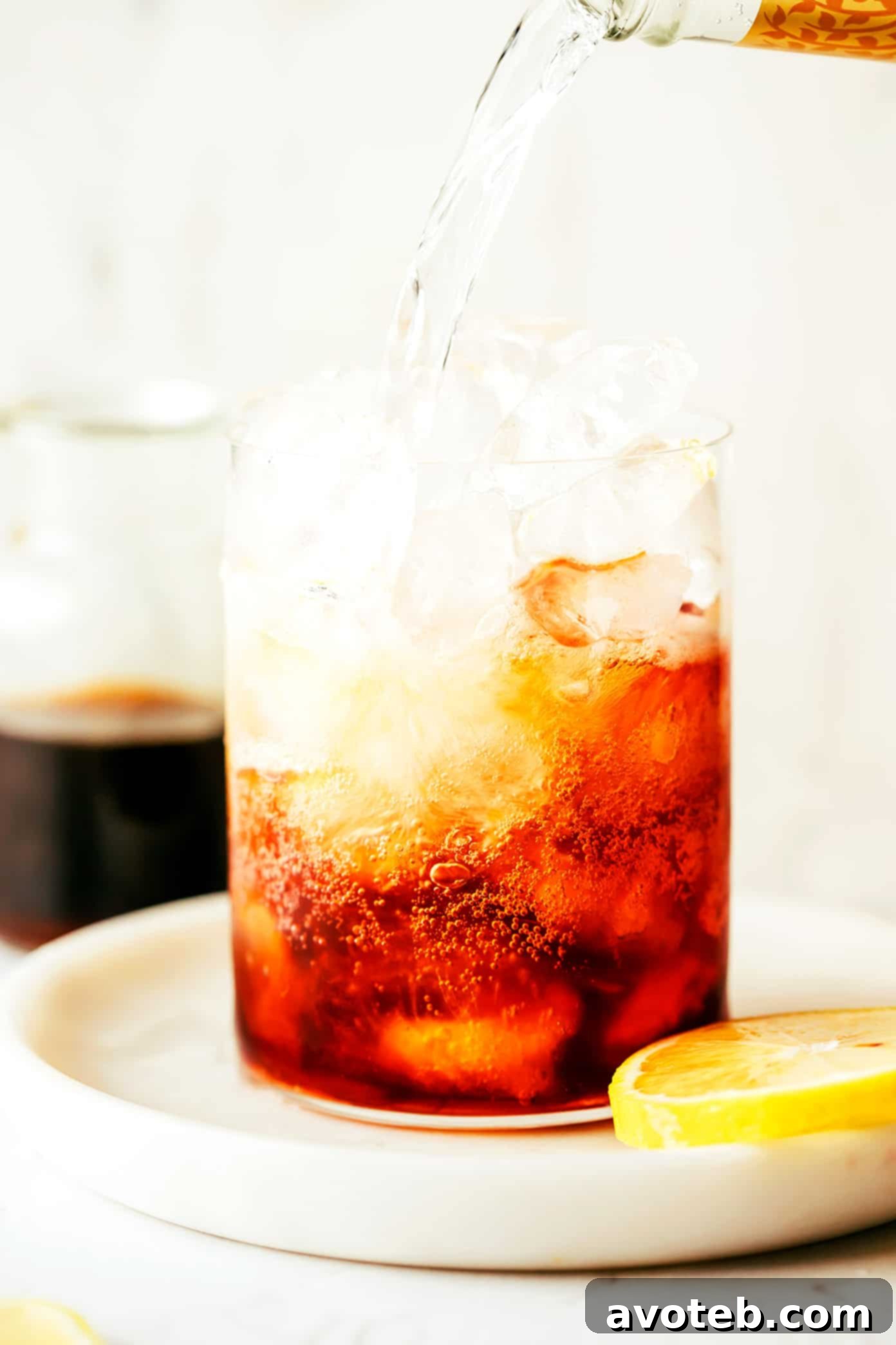 A hand pouring tonic water into a glass filled with cold brew concentrate and ice, showing the effervescence.