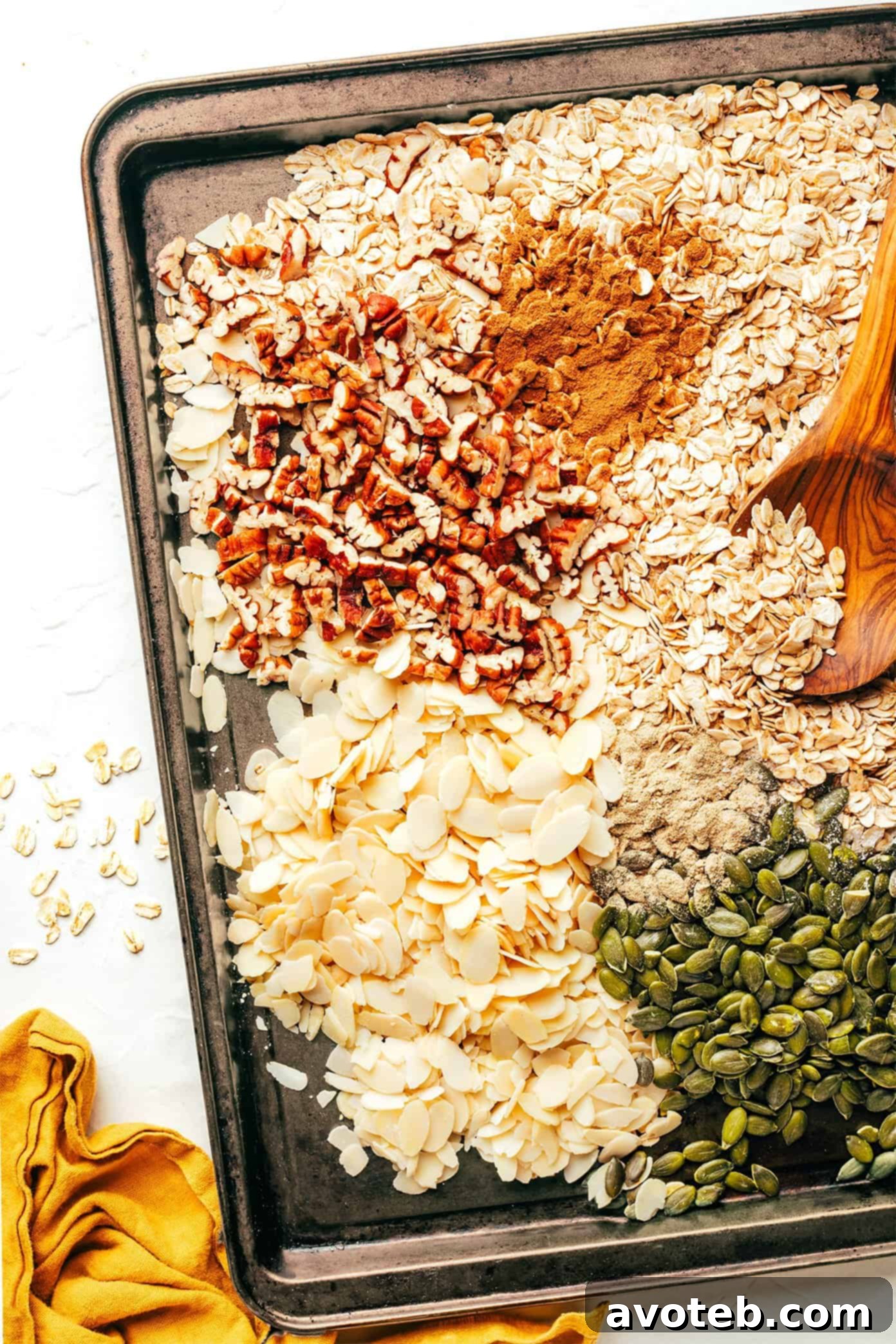 This delicious homemade muesli recipe is easy to make and customize with your favorite blend of oats, nuts, seeds, dried fruit, coconut (optional) and spices. Serve with hot or cold milk, prep "overnight oats"-style, layer as a parfait with Greek yogurt, or however you love best. Always such a great healthy and easy breakfast! | gimmesomeoven.com Raw old-fashioned oats, sliced almonds, pepitas, and chopped pecans mixed with cinnamon, cardamom, and sea salt, spread evenly on a baking sheet, ready for toasting to enhance their flavor and crunch.